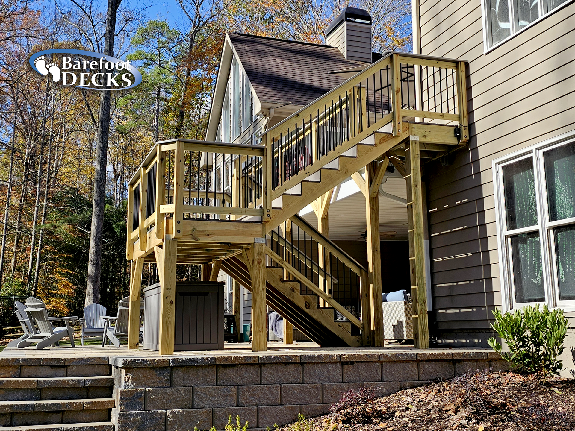 Wooden deck with stairs attached to a house with a stone retaining wall.