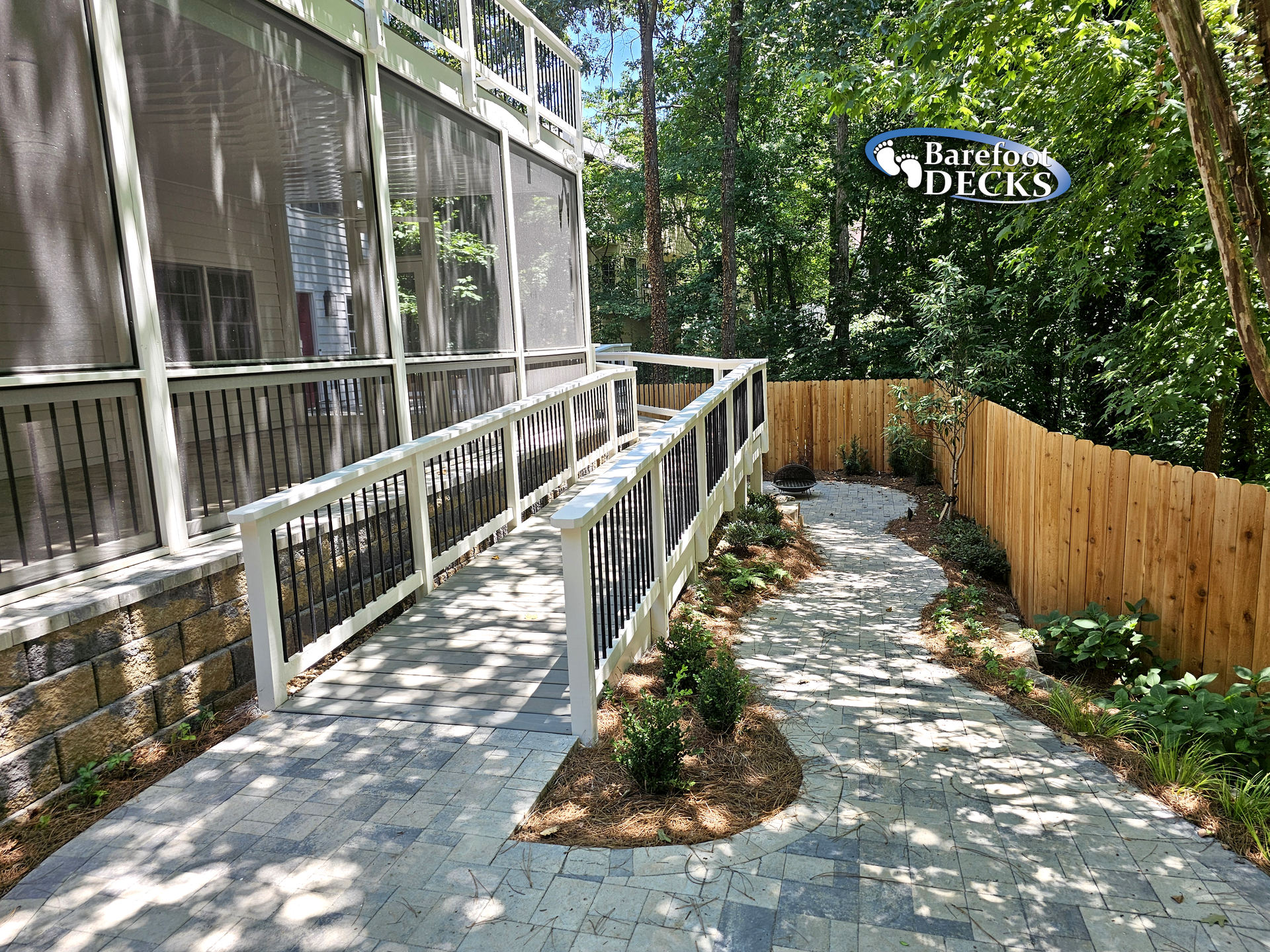 A brick pathway with a wheelchair ramp leading to a screened porch, next to a wooden fence.