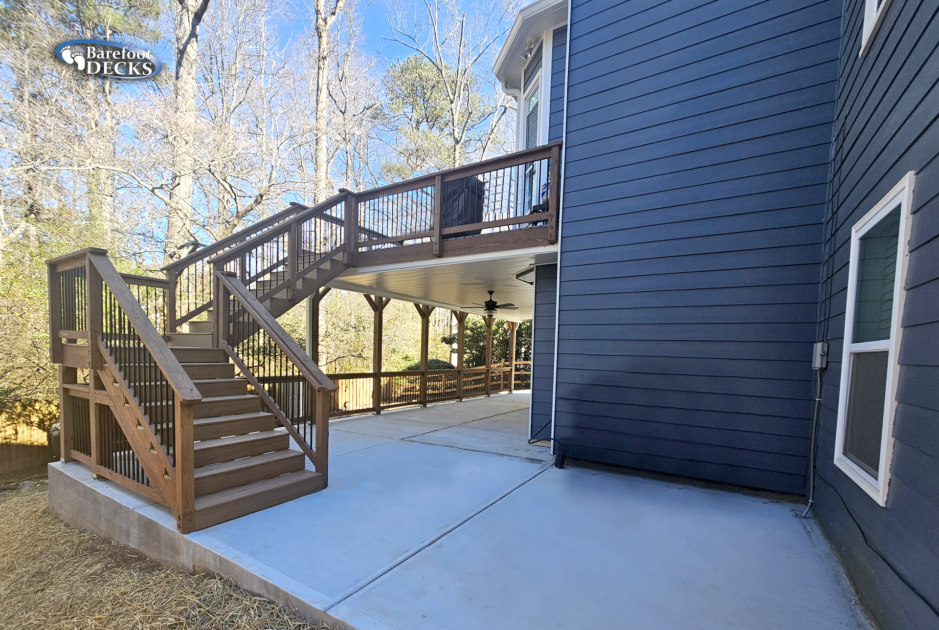 Wooden deck with stairs leading to a second-story deck, adjacent to a dark blue house.