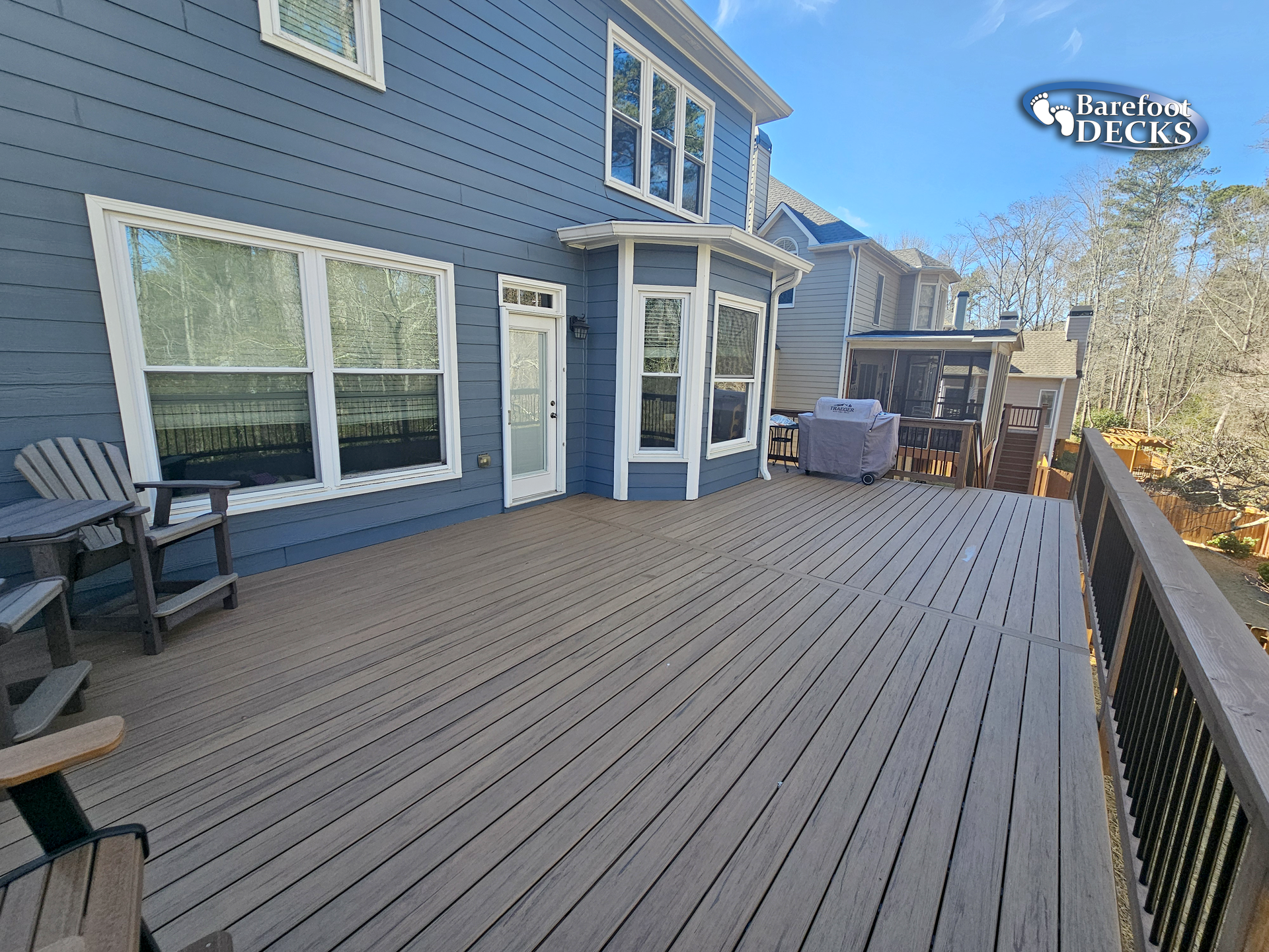 A wooden deck extends from a blue house with multiple windows and a chair.