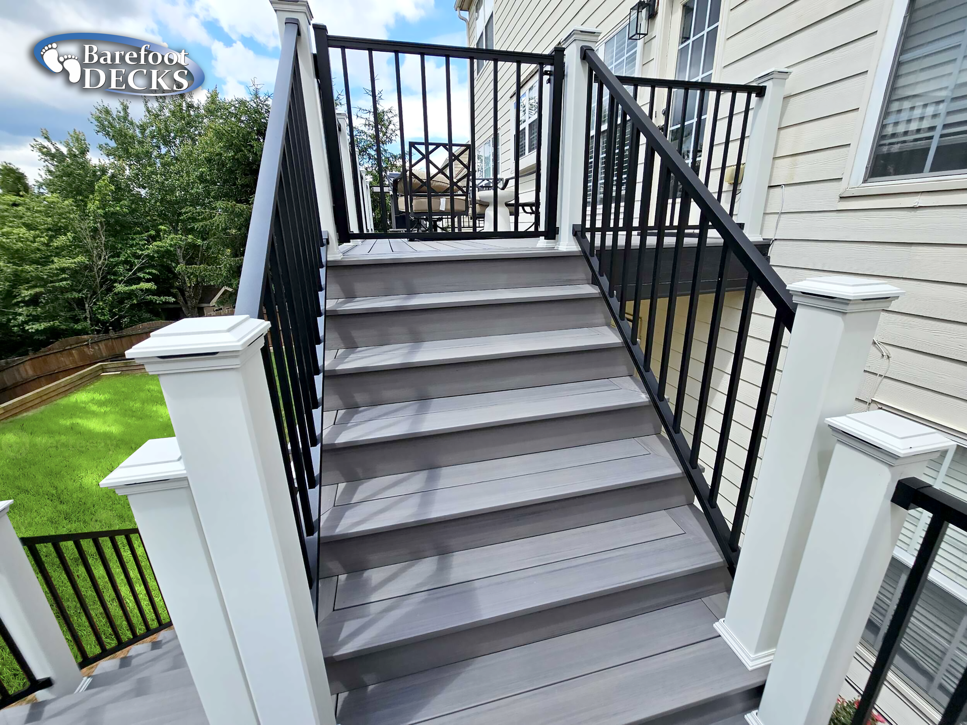 Gray deck stairs with black railings leading up to a platform. White posts frame the steps.