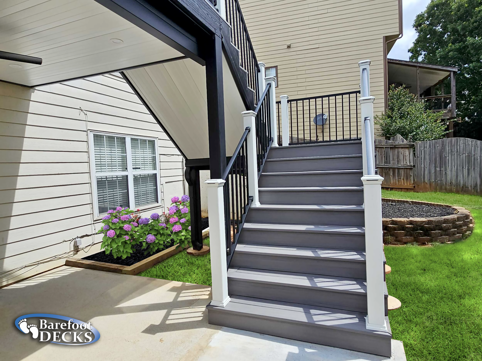 A gray deck with stairs leading to a backyard with a black railing and white posts.