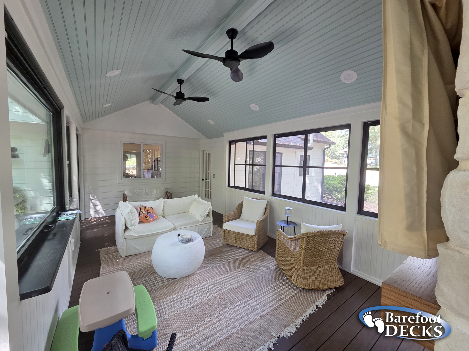 Sunroom with white walls, blue ceiling, dark trim, wicker chairs, and neutral rug.