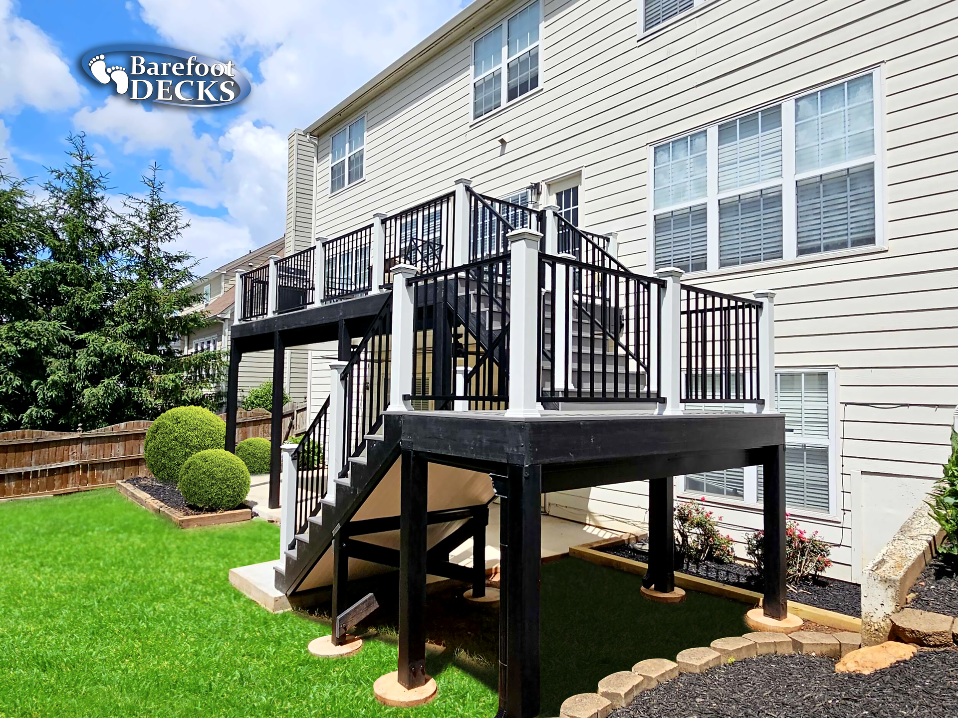 Multi-level deck with black railing and white posts, built in backyard.