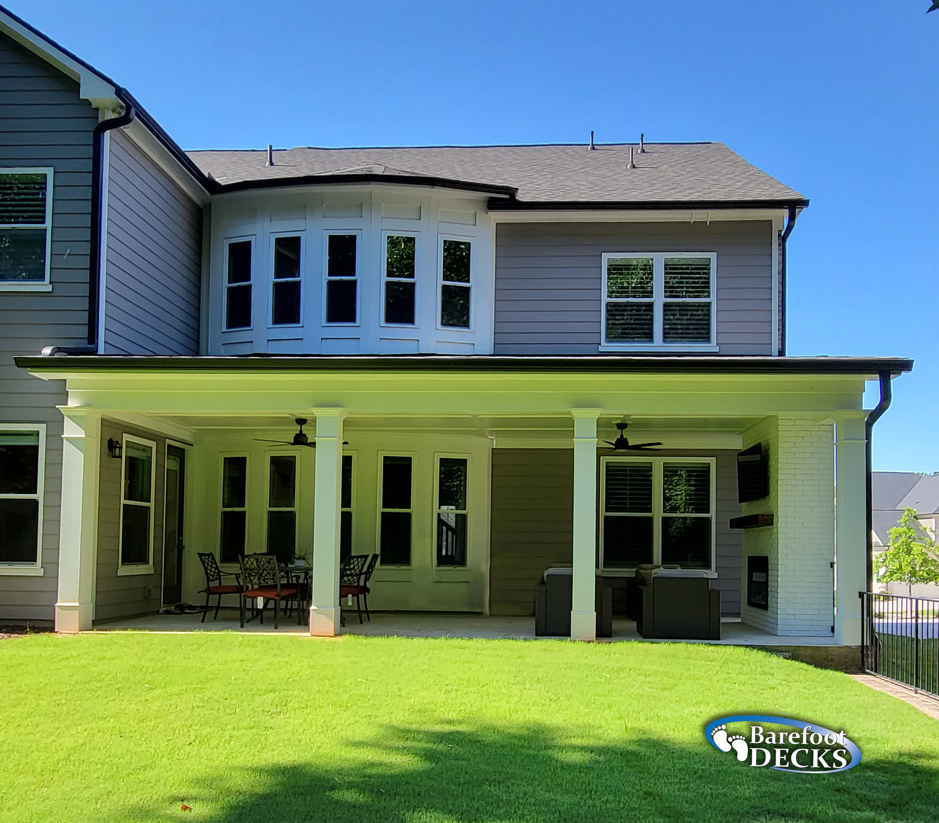 Backyard patio with columns, green grass, and a two-story house with blue siding.