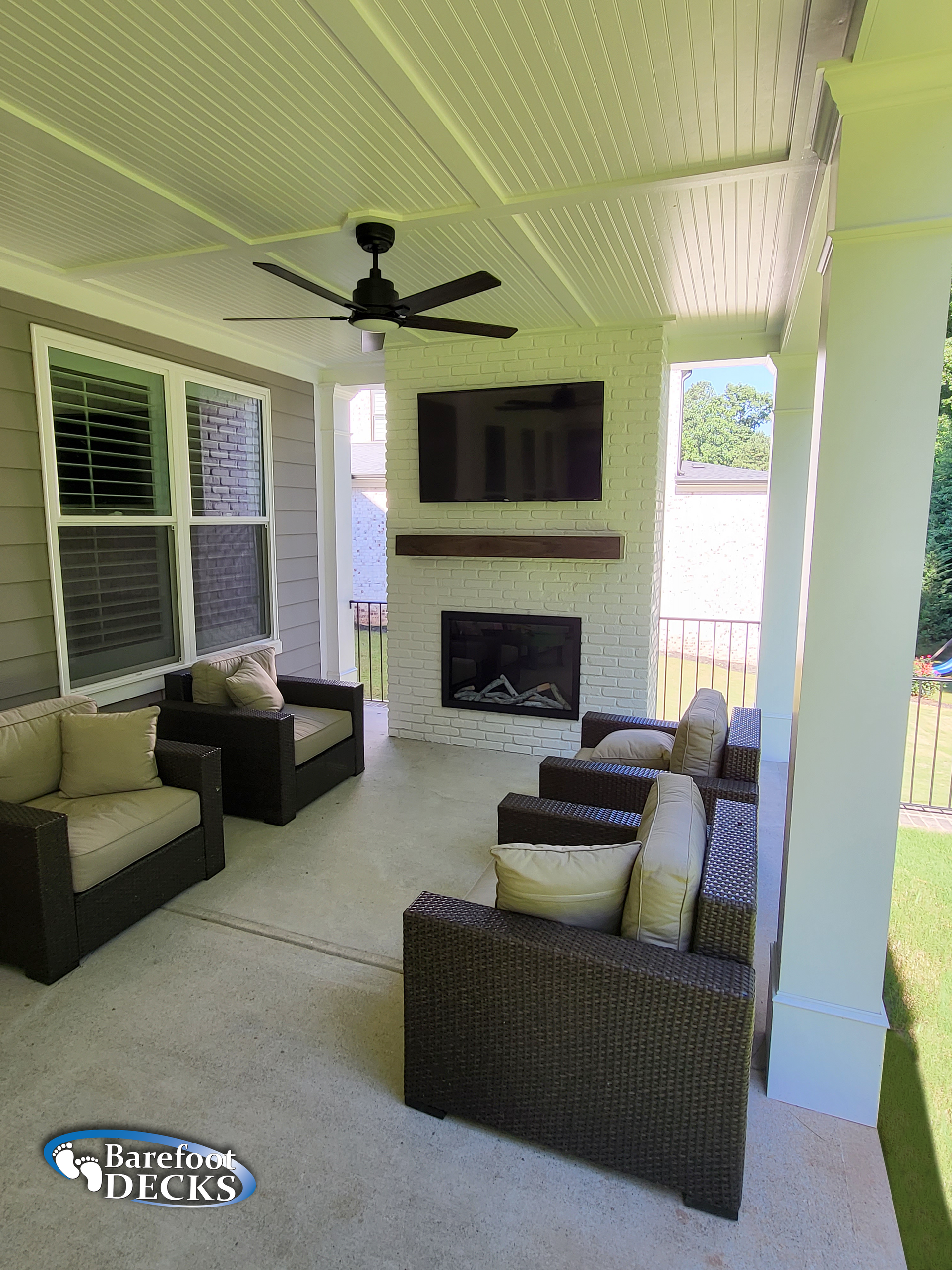 Covered patio with seating, fireplace, TV, and ceiling fan.