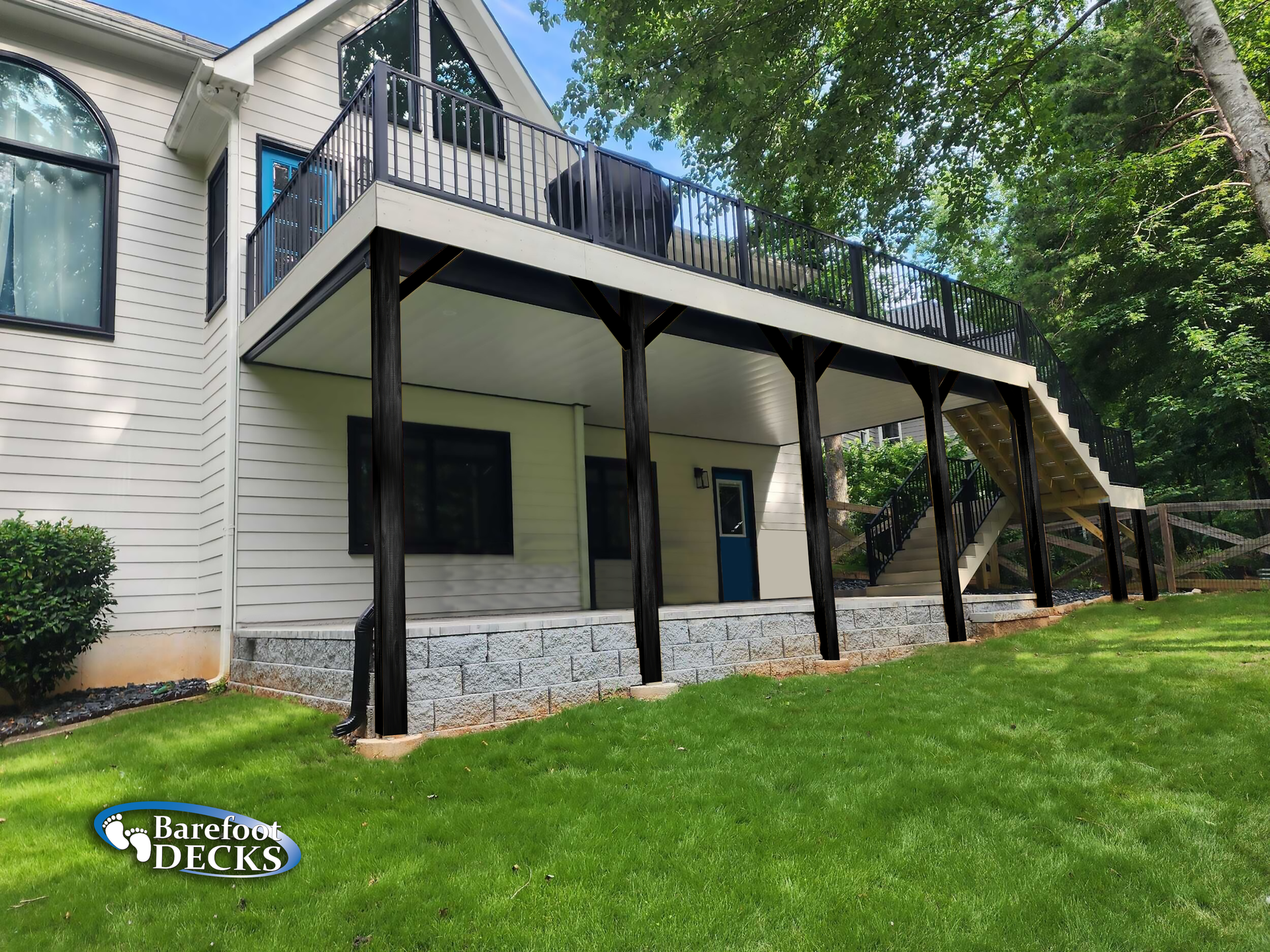 A two-story deck on the back of a house with black posts, stairs, and railing, overlooking a green lawn.