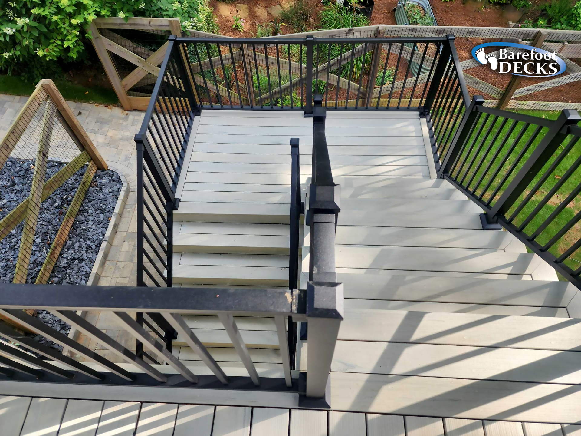 Gray deck with black railing and steps leading down. A small garden is visible on the left.