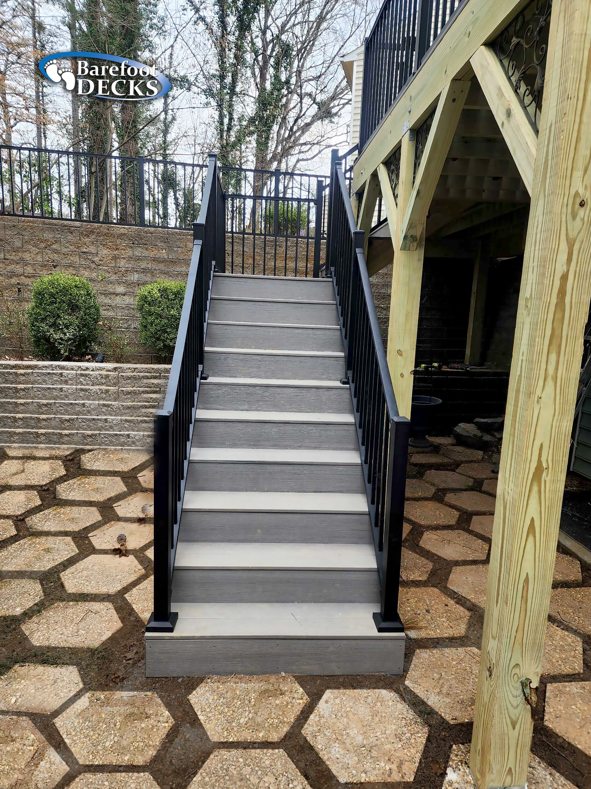 Staircase with black railings leading up to a deck; path of hexagonal pavers below.