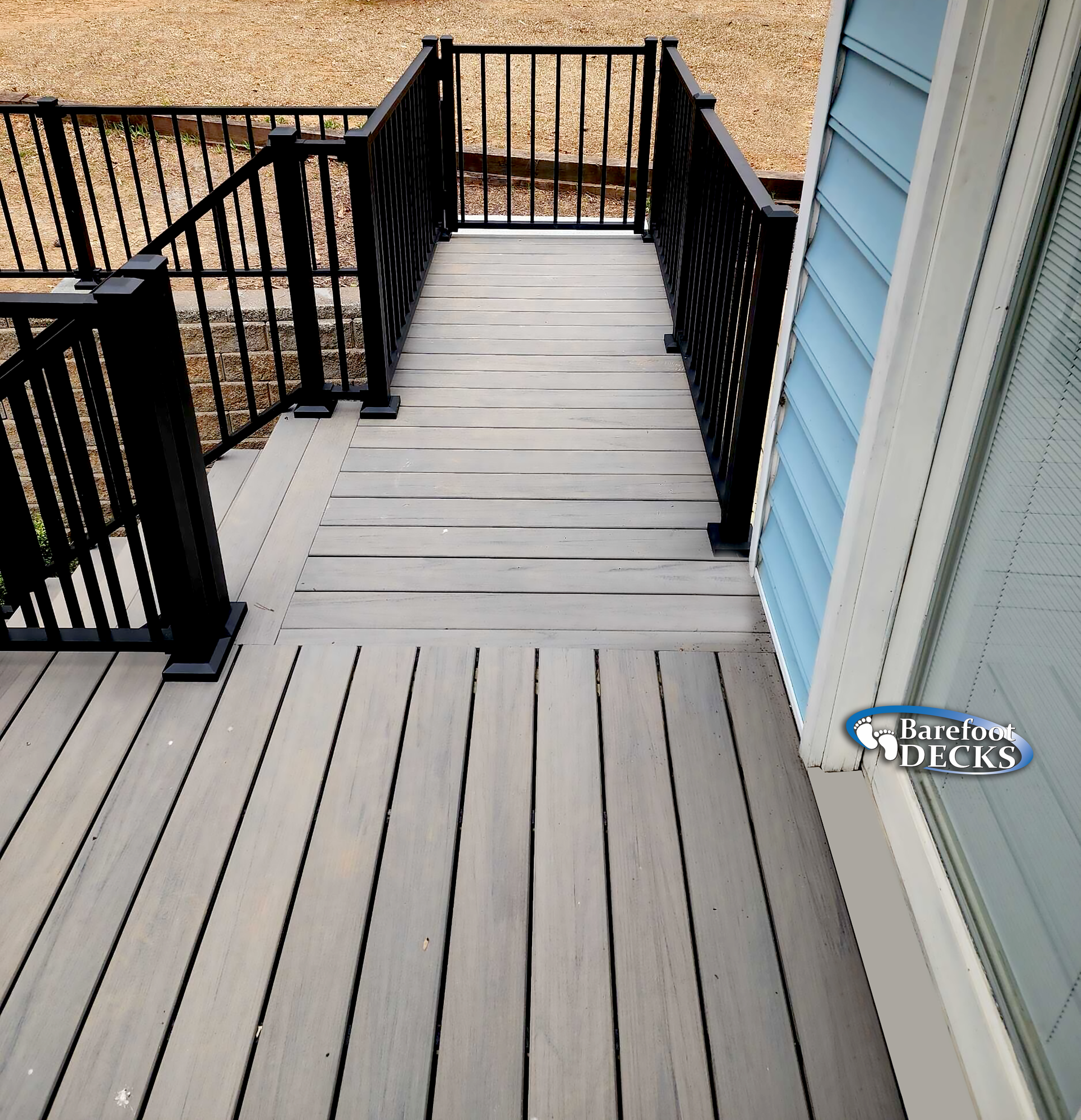 Wooden deck with black railing and steps, leading to a house with blue siding.