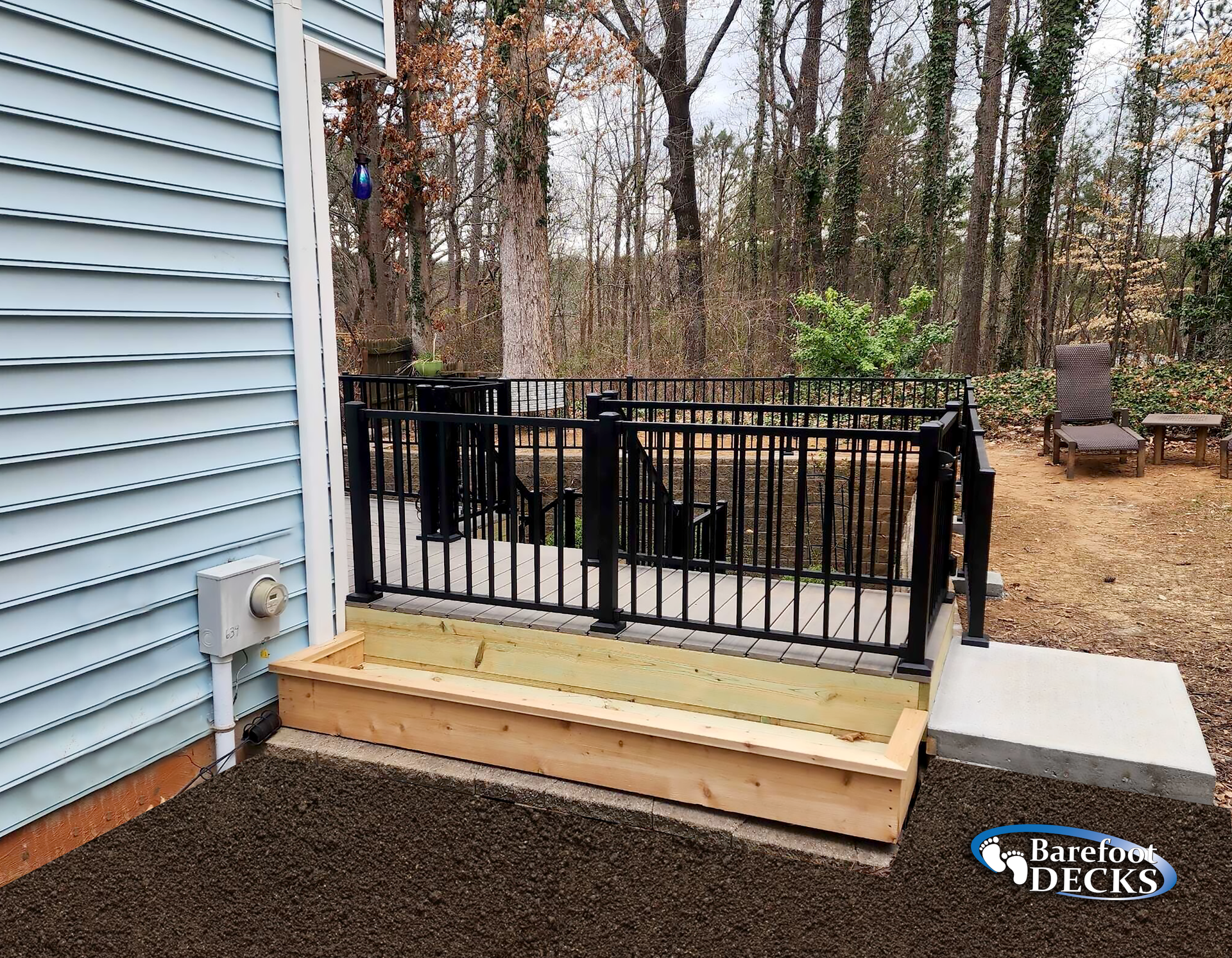 Outdoor deck with black railing, wooden planter, and steps near a house with blue siding.