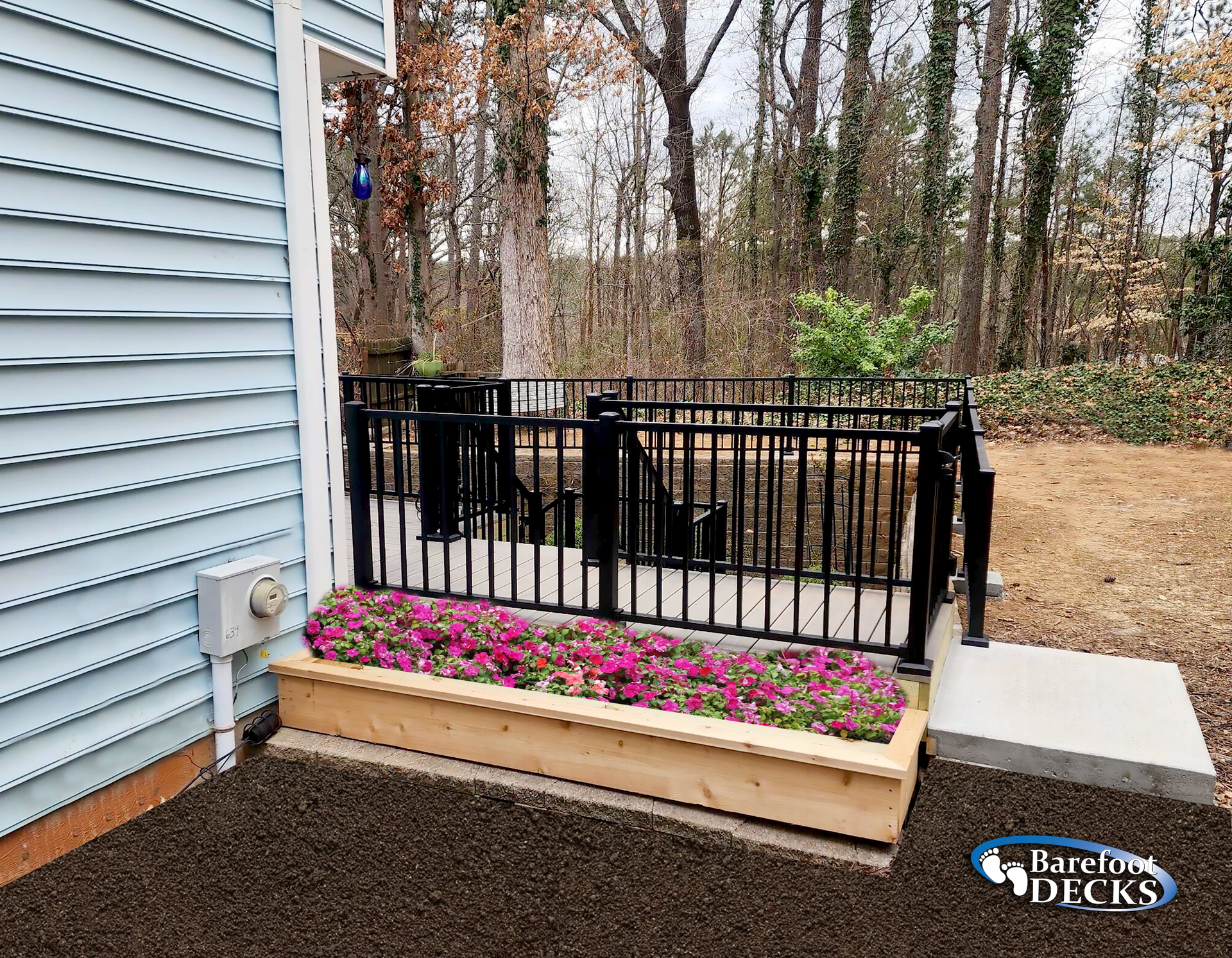 A small deck with black railing and pink flowers in a wooden planter against a blue house.