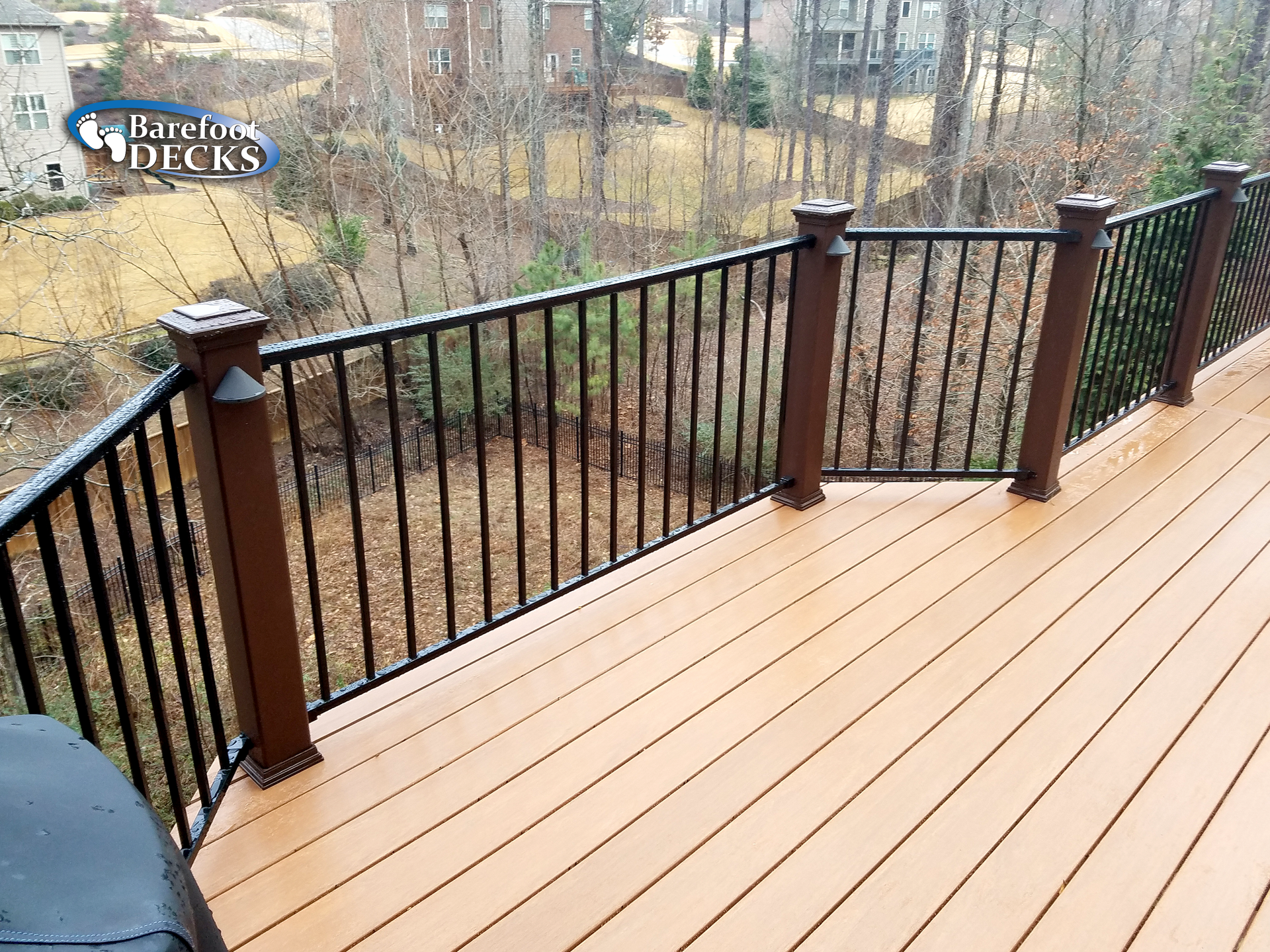 Brown deck with black railing and brown posts overlooking a wooded area.