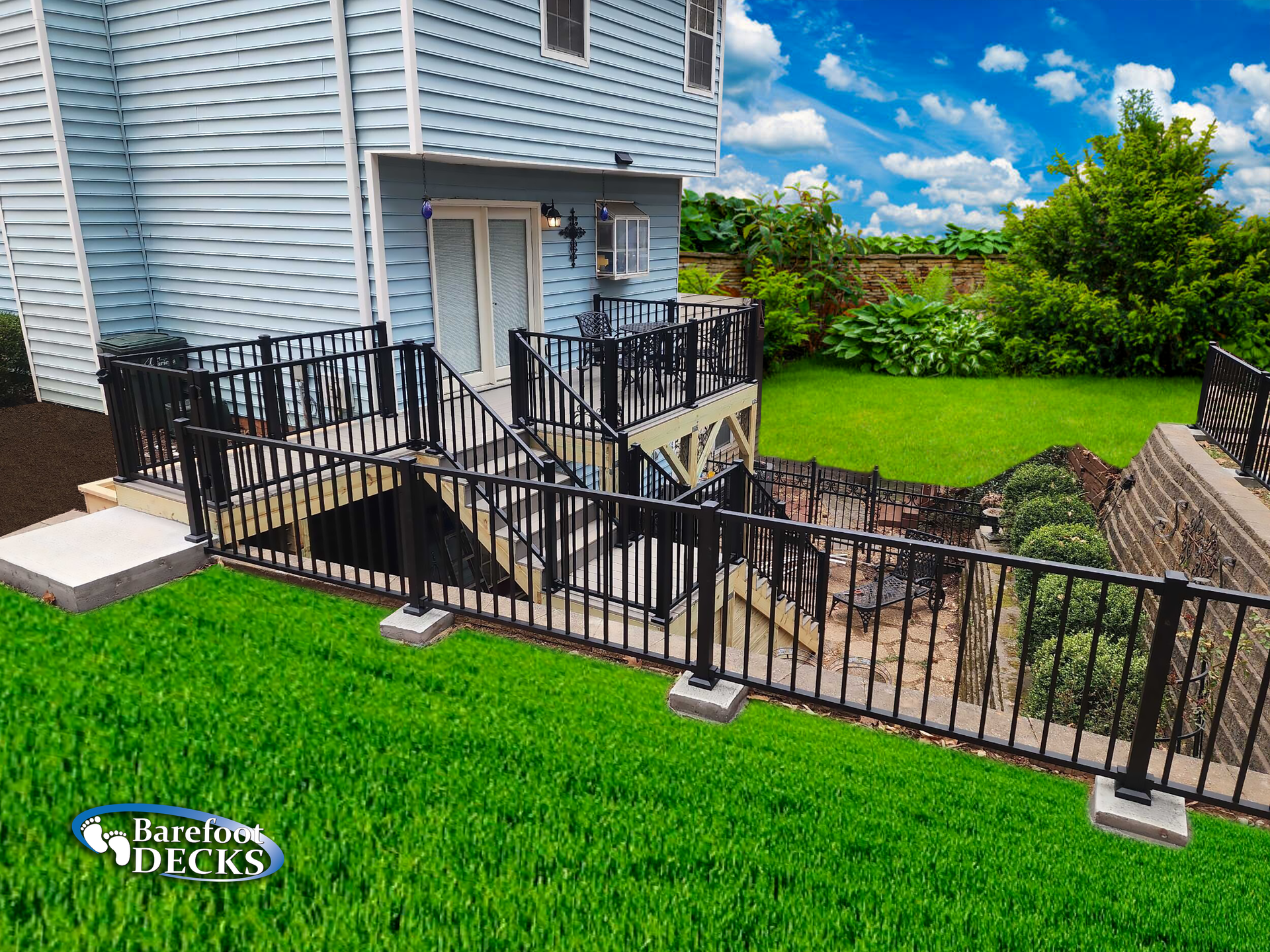 Black railed deck and stairs on a grassy slope, leading down to a lower level, against a light blue house.