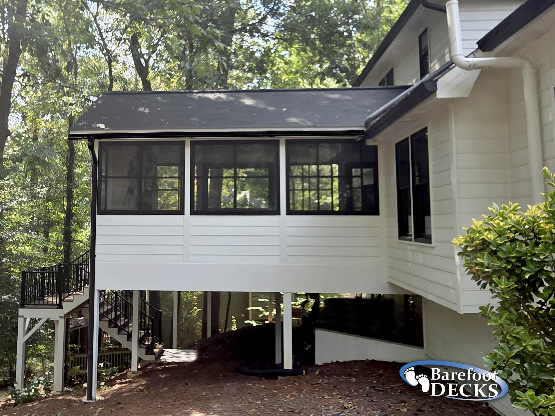White elevated porch with screened windows attached to a two-story white house surrounded by trees.