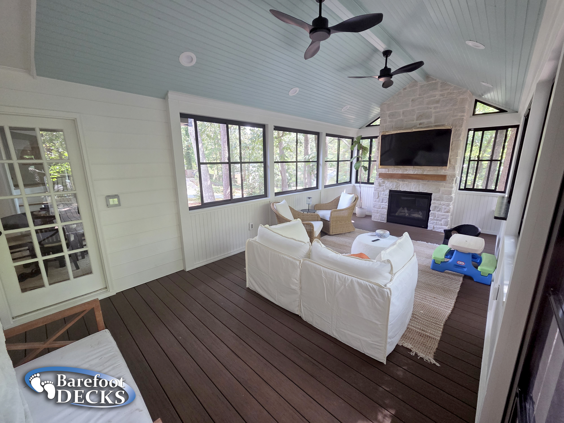 Cozy sunroom with dark wood floors, white walls, stone fireplace, and light blue ceiling.