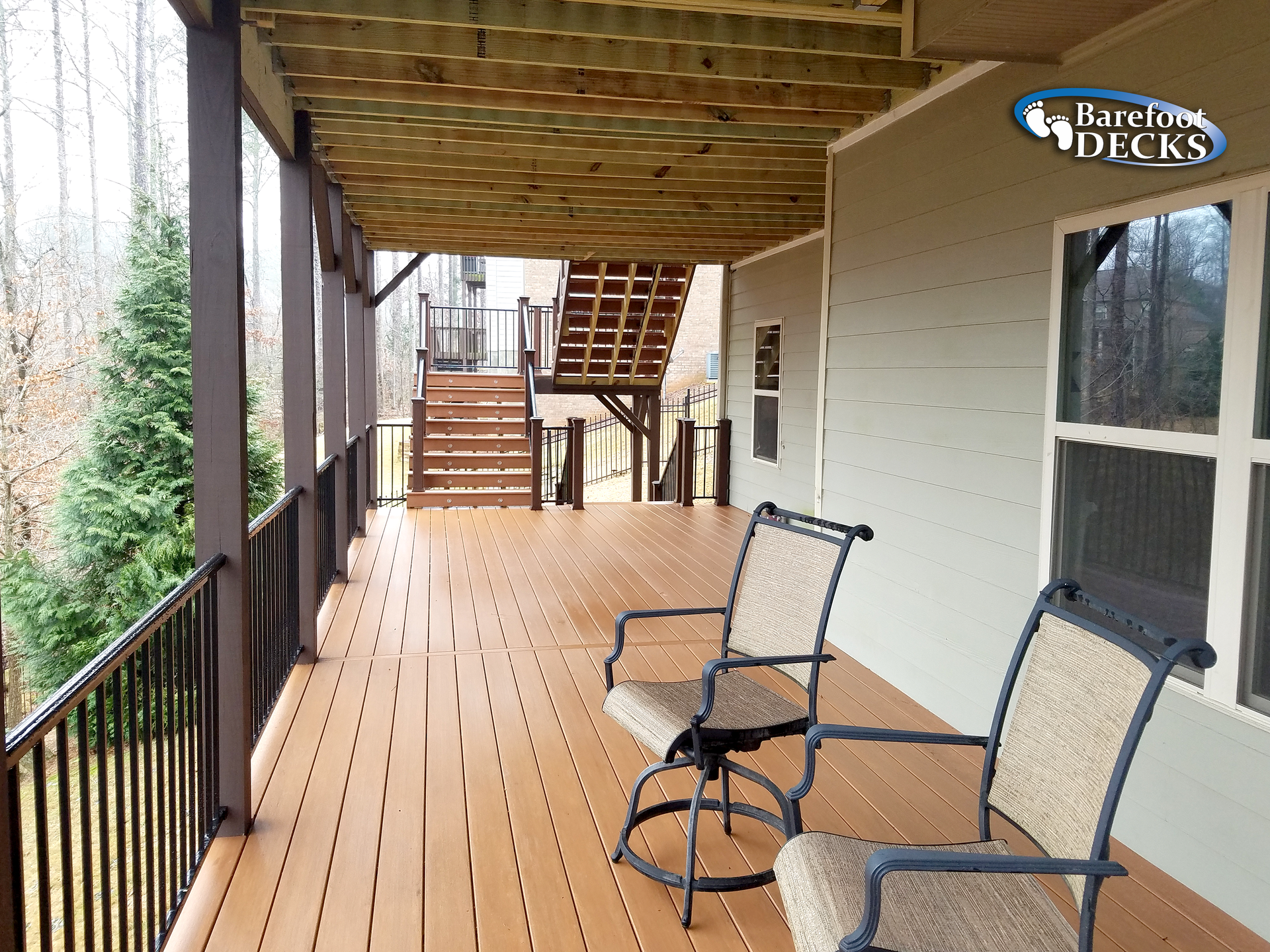 Deck with two chairs overlooking a wooded area. The deck has stairs leading up.