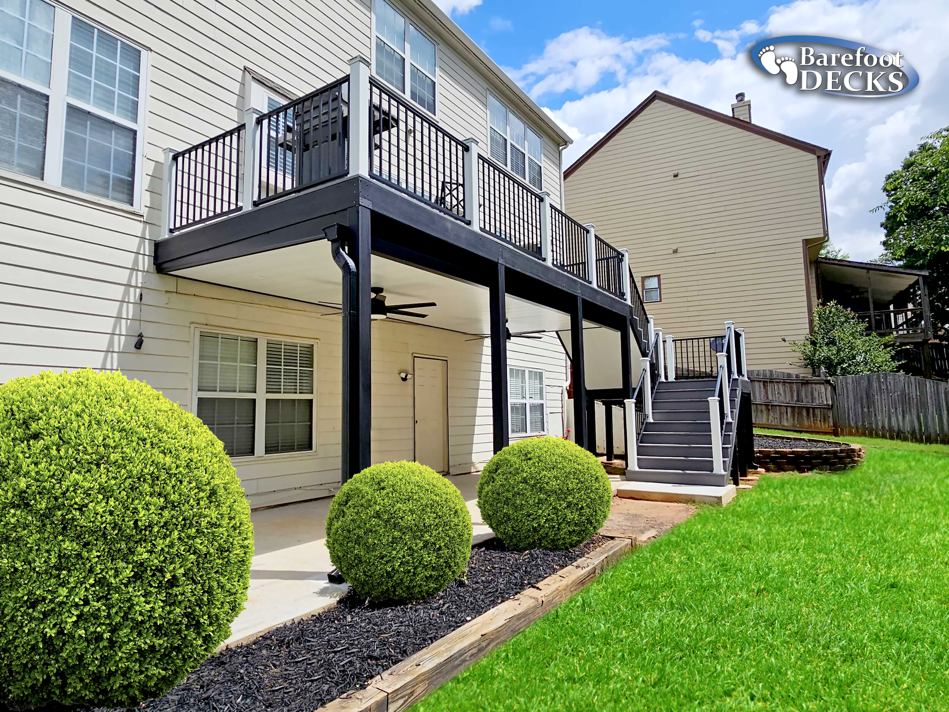 Black and white elevated deck with stairs and black and white railing, near a house with bushes in the lawn.