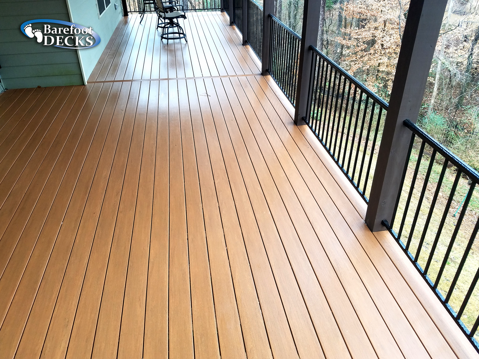 A wide brown composite deck with black railing overlooking a wooded area.