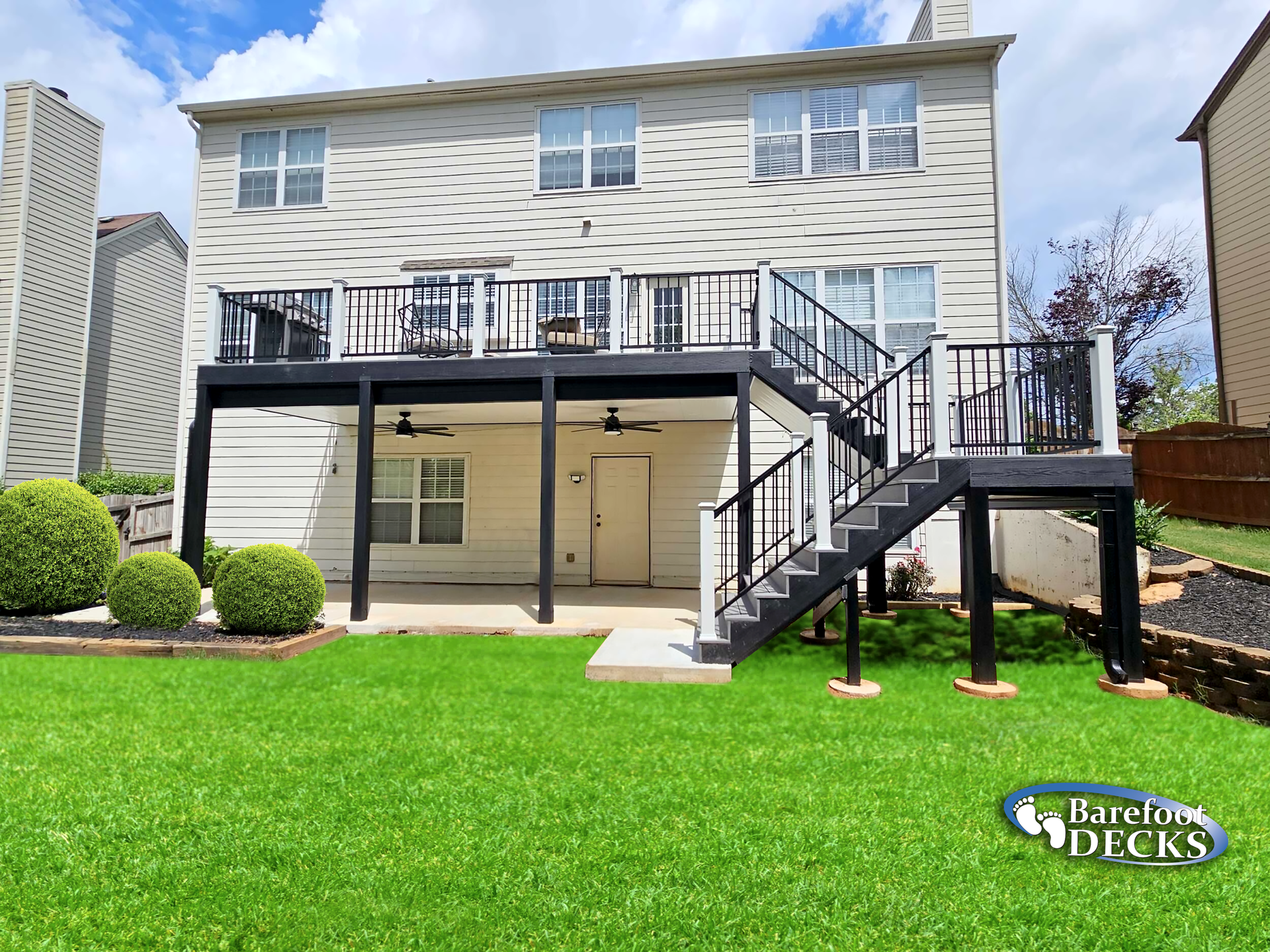 Two-story house with black and white deck, stairs, and backyard lawn.