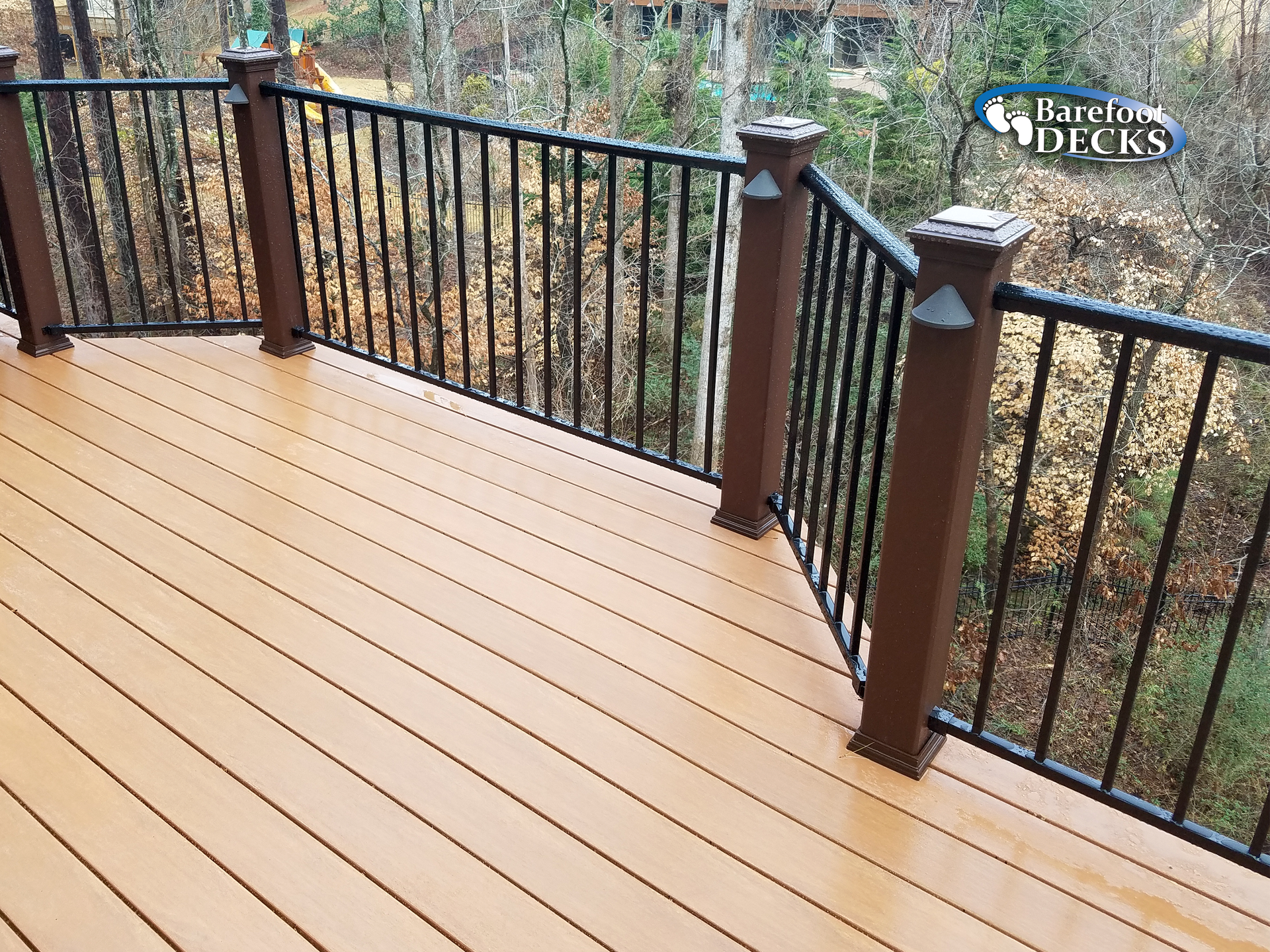 Brown composite deck with black railing and brown posts. Forest in the background.