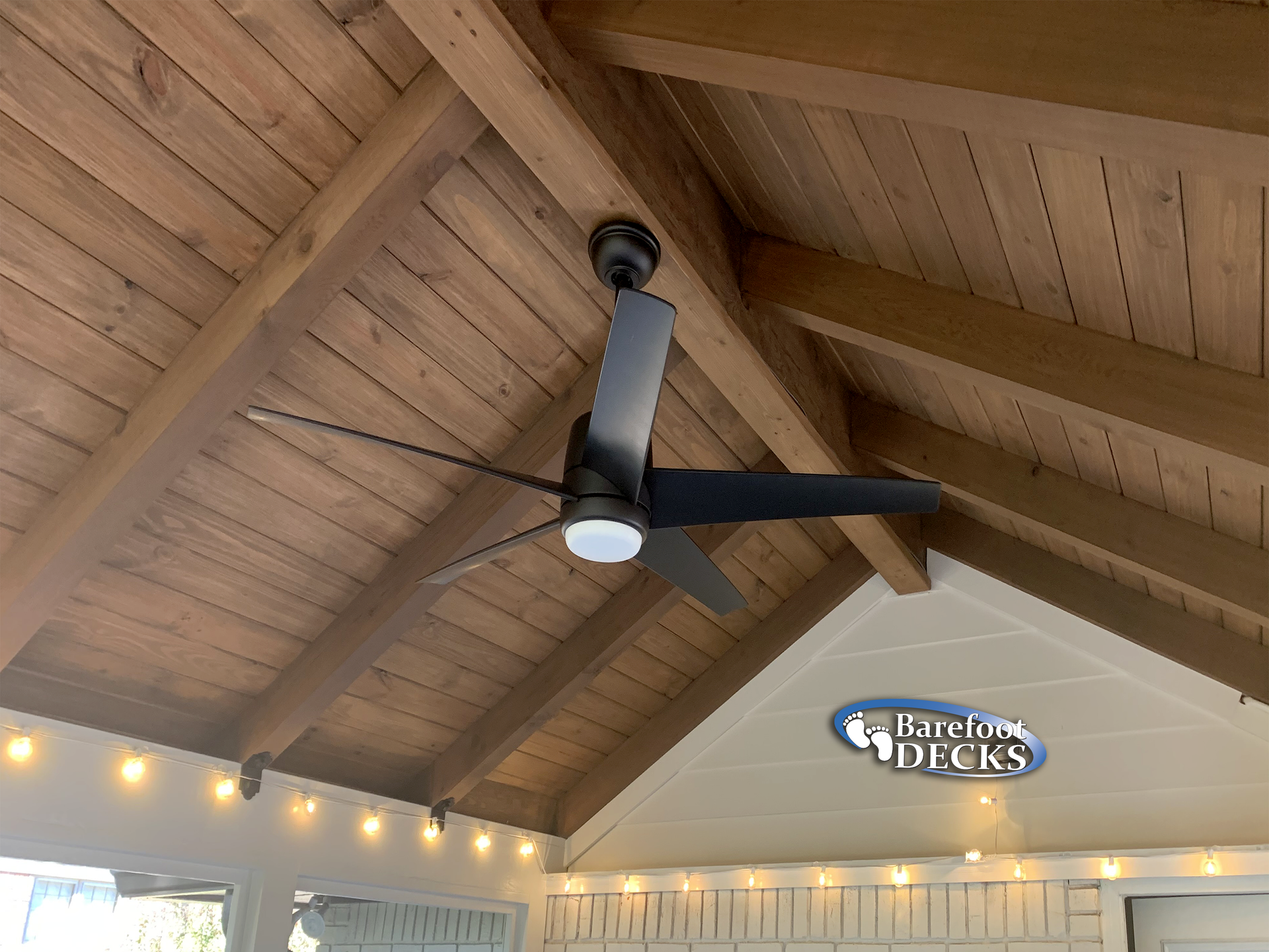 Ceiling fan under a wood-beamed roof, with string lights.