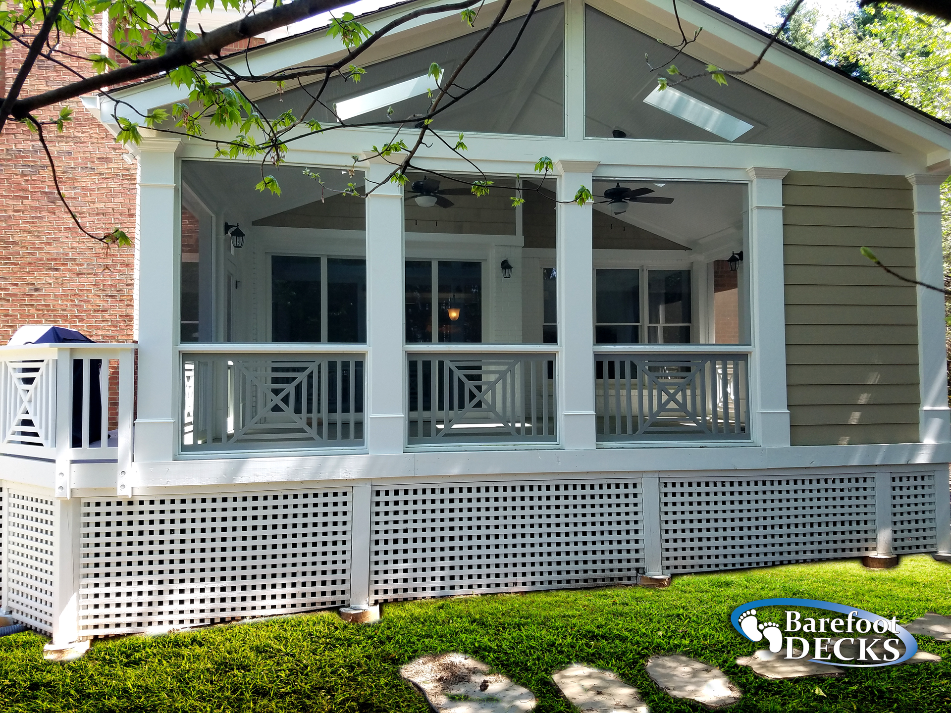 Screened-in porch with white latticework, columns, and railing; tan siding; built on a deck in a yard.
