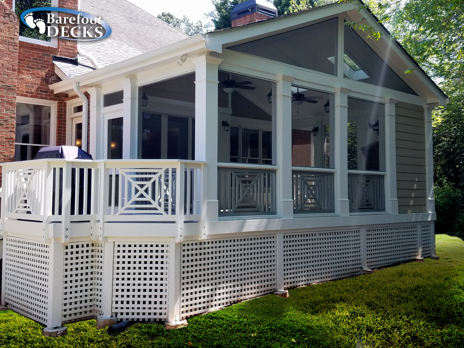 White screened porch attached to a brick house with a lattice base and deck.