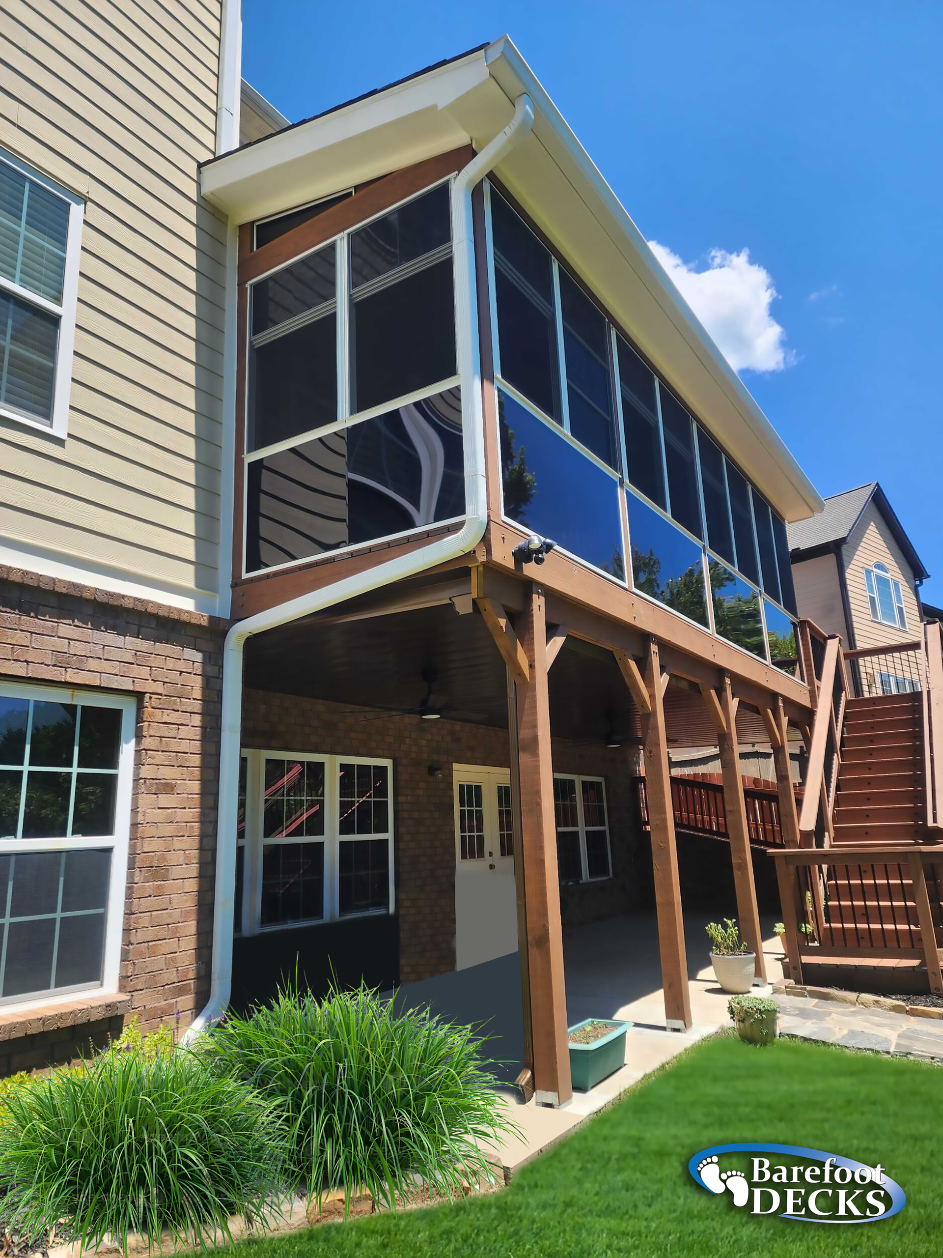 Screened-in porch attached to a house with a brick and siding exterior, brown frame, and wooden stairs.