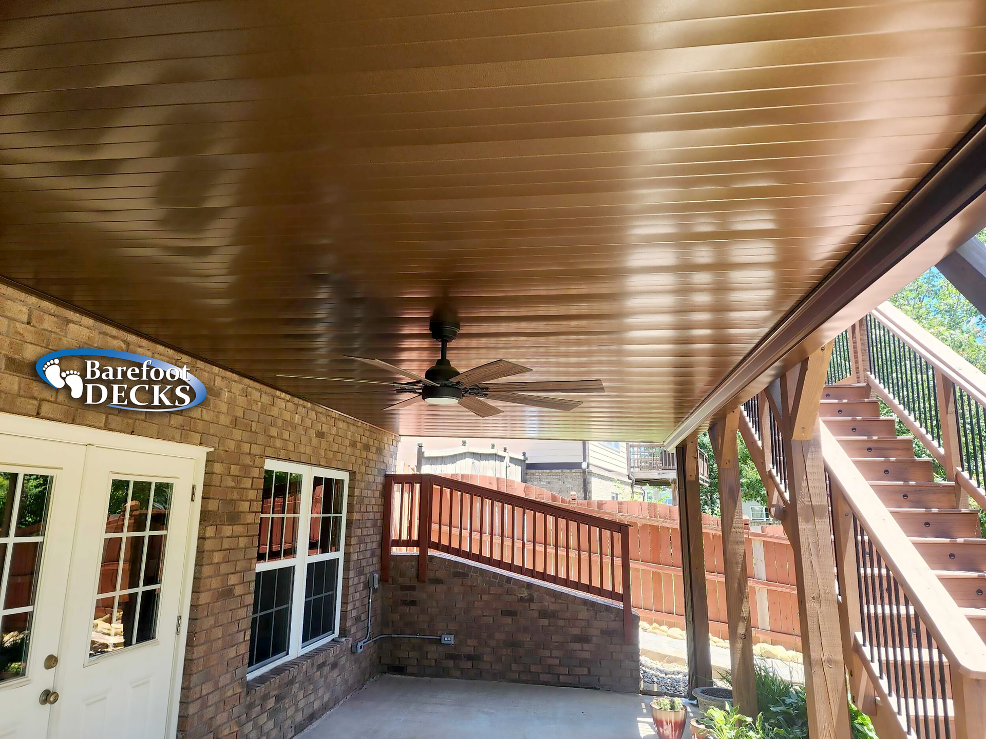 Covered deck with ceiling fan, brick wall, and stairs leading up.
