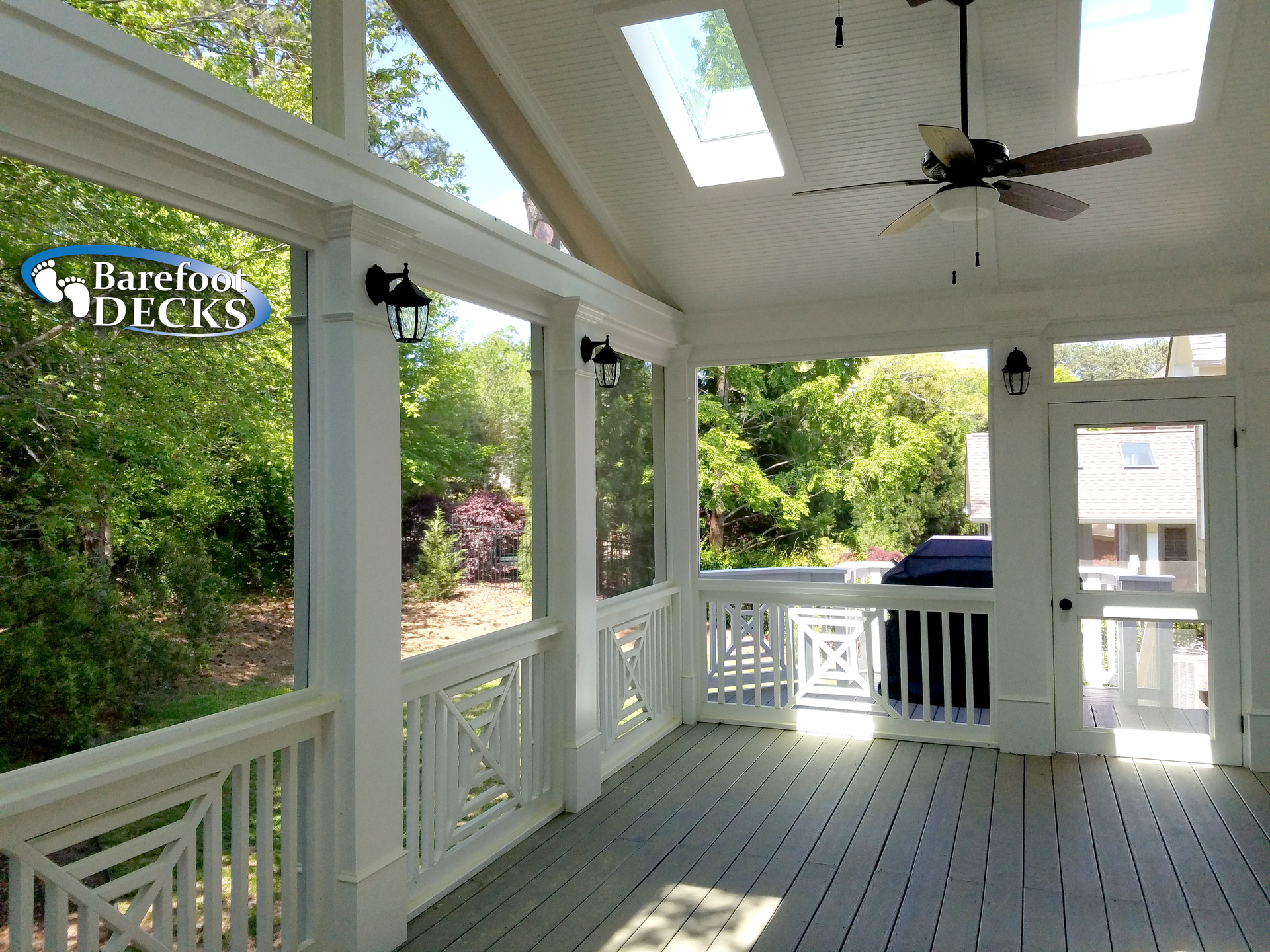 Screened porch with white railings and ceiling, skylights, and a ceiling fan, overlooking a yard.