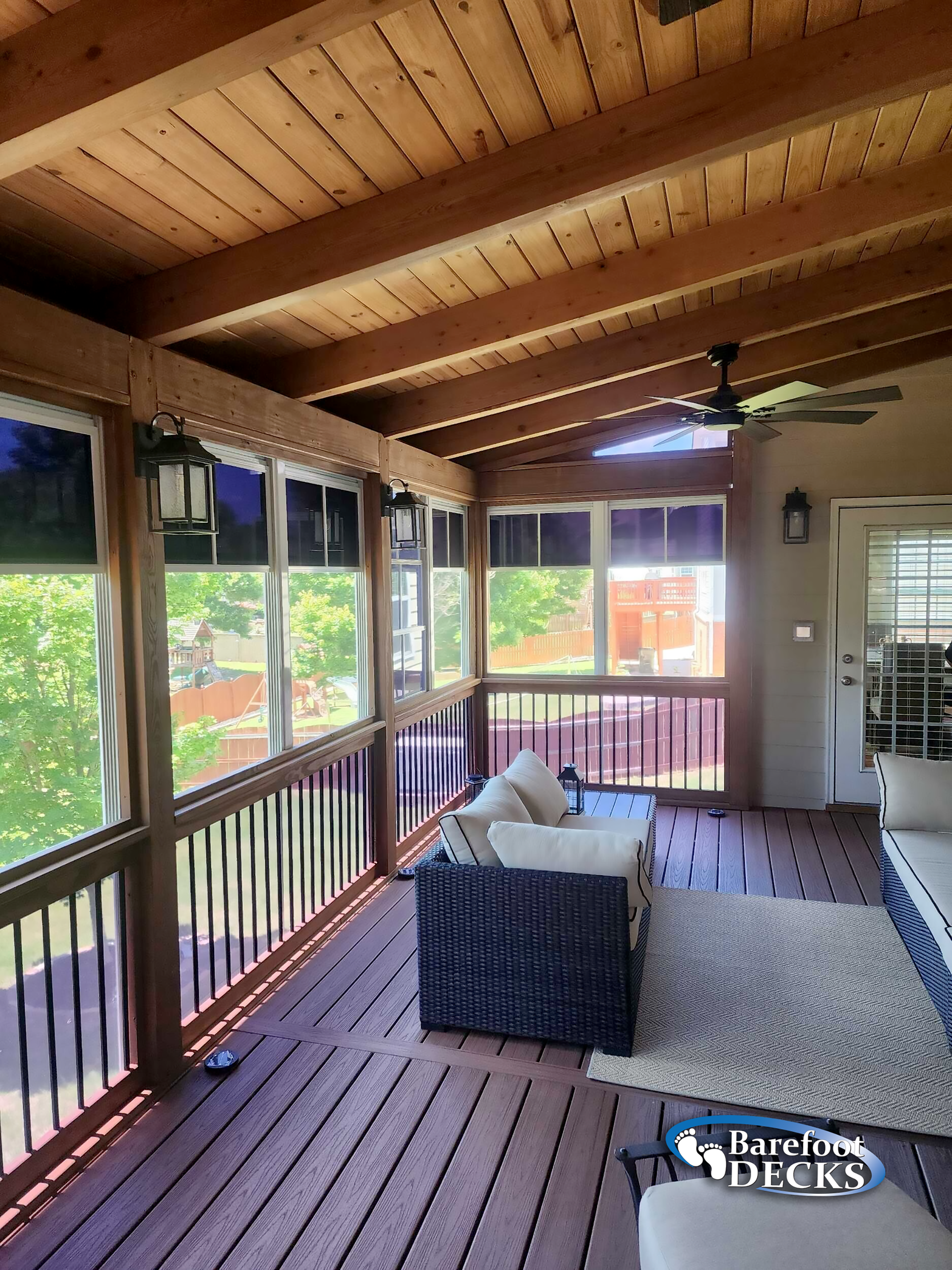 Screened porch with dark wood deck, white furniture, and a rug. Ceiling fan and lanterns visible.