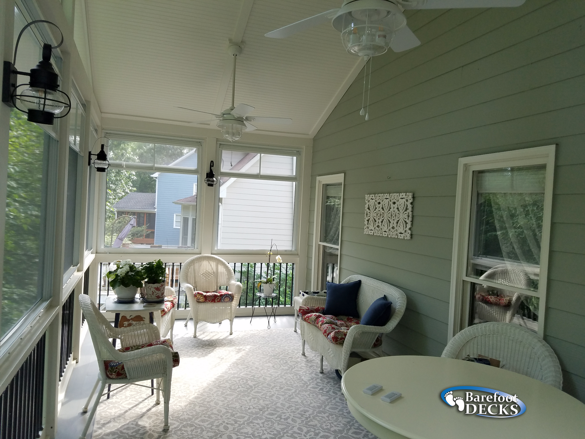 Screened-in porch with white wicker furniture, green walls, and ceiling fans.