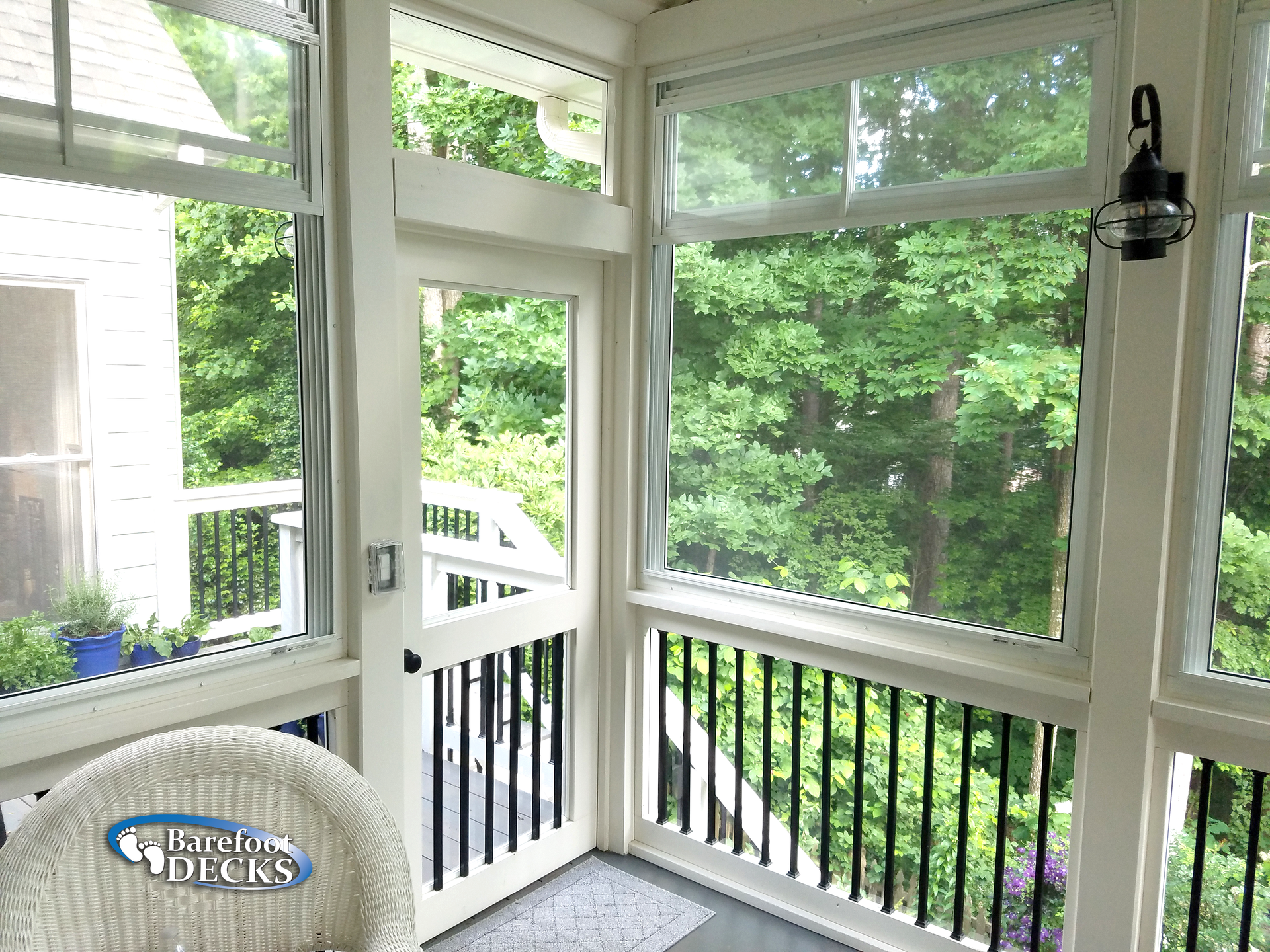 Screened porch with white trim, black railings, and a view of green trees. A white chair is in the foreground.