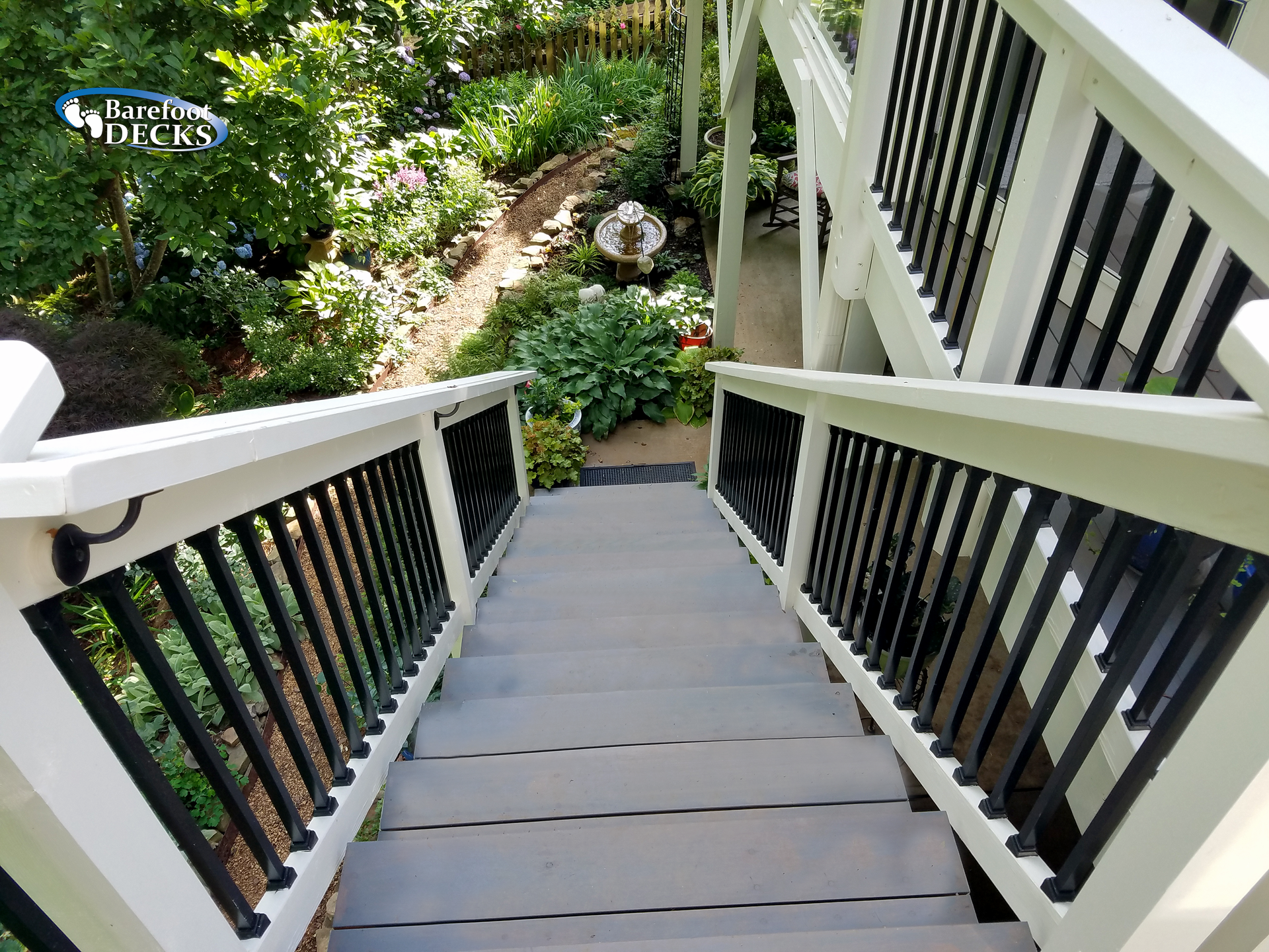 Staircase leading down to a garden. Gray steps, white railings, black balusters. Overlook perspective.