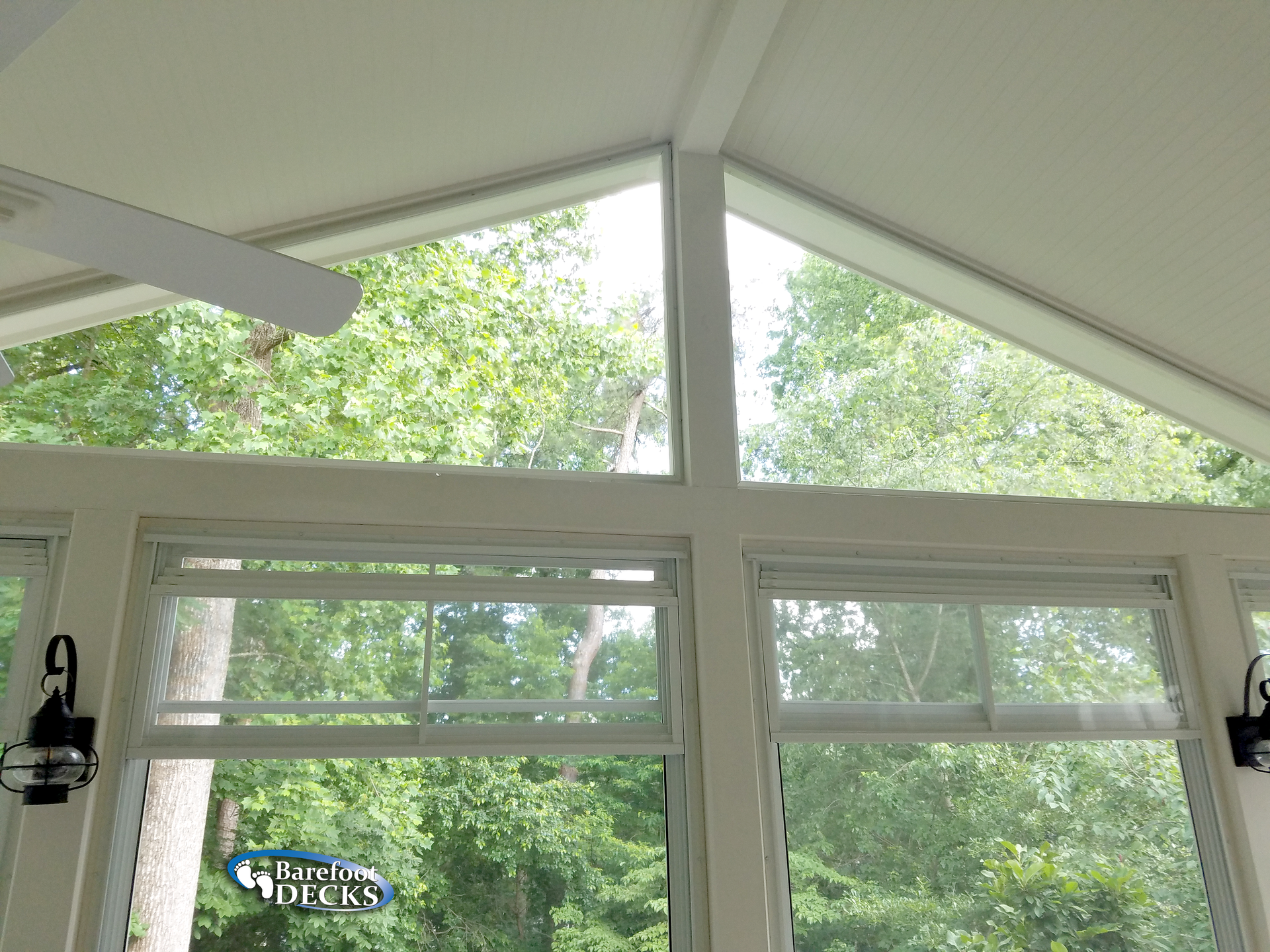 White-framed windows in a sunroom with a peaked ceiling, overlooking green trees.