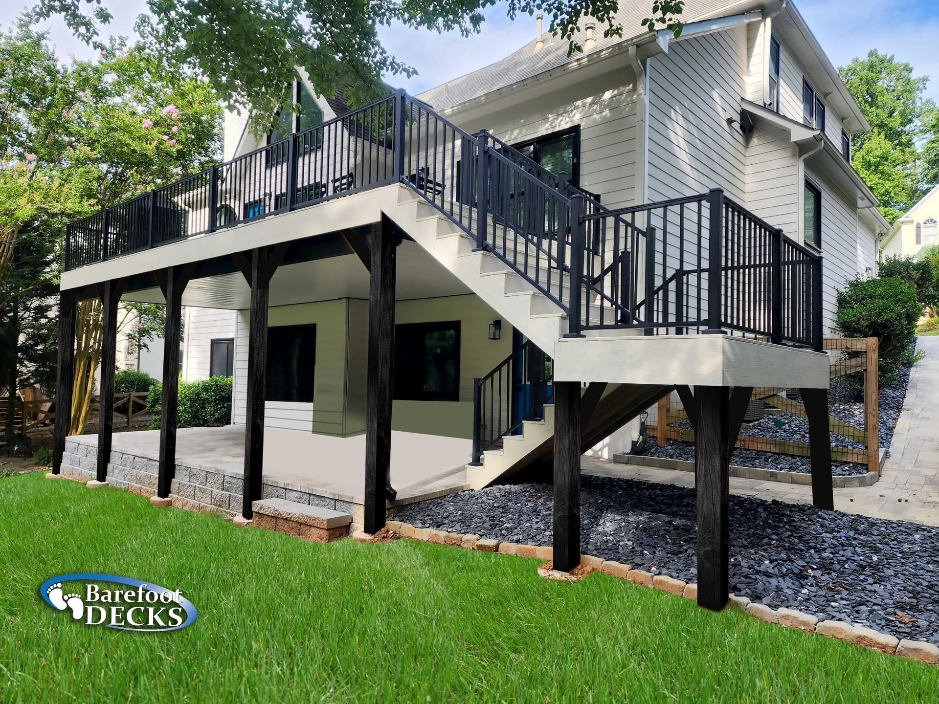Multi-level deck with black railing and supports attached to a white house with landscaping.