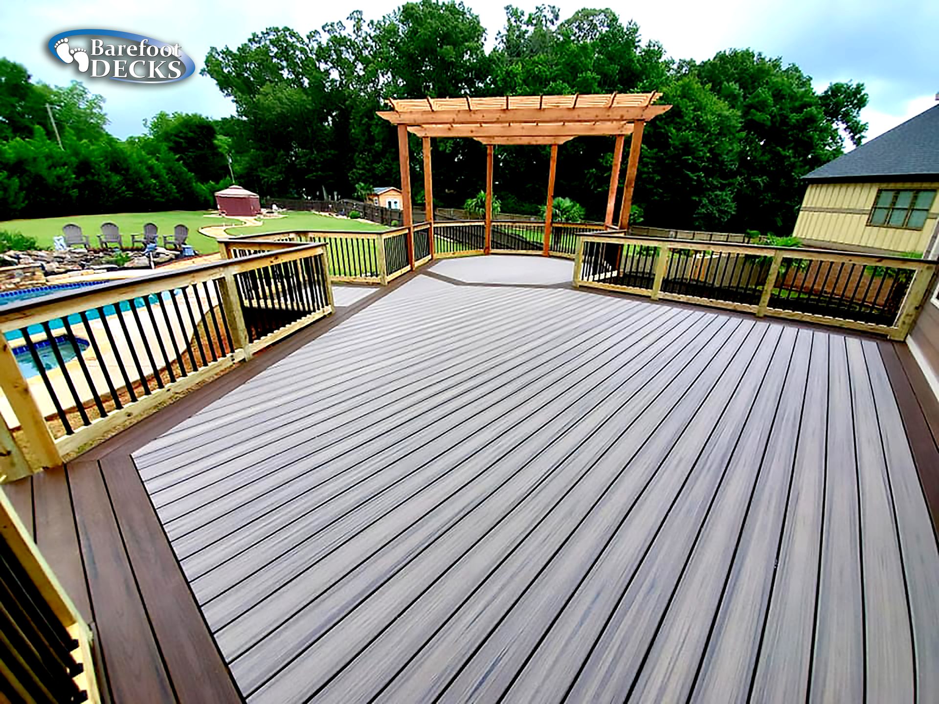 Wooden deck with pergola, overlooking a pool and yard with trees.