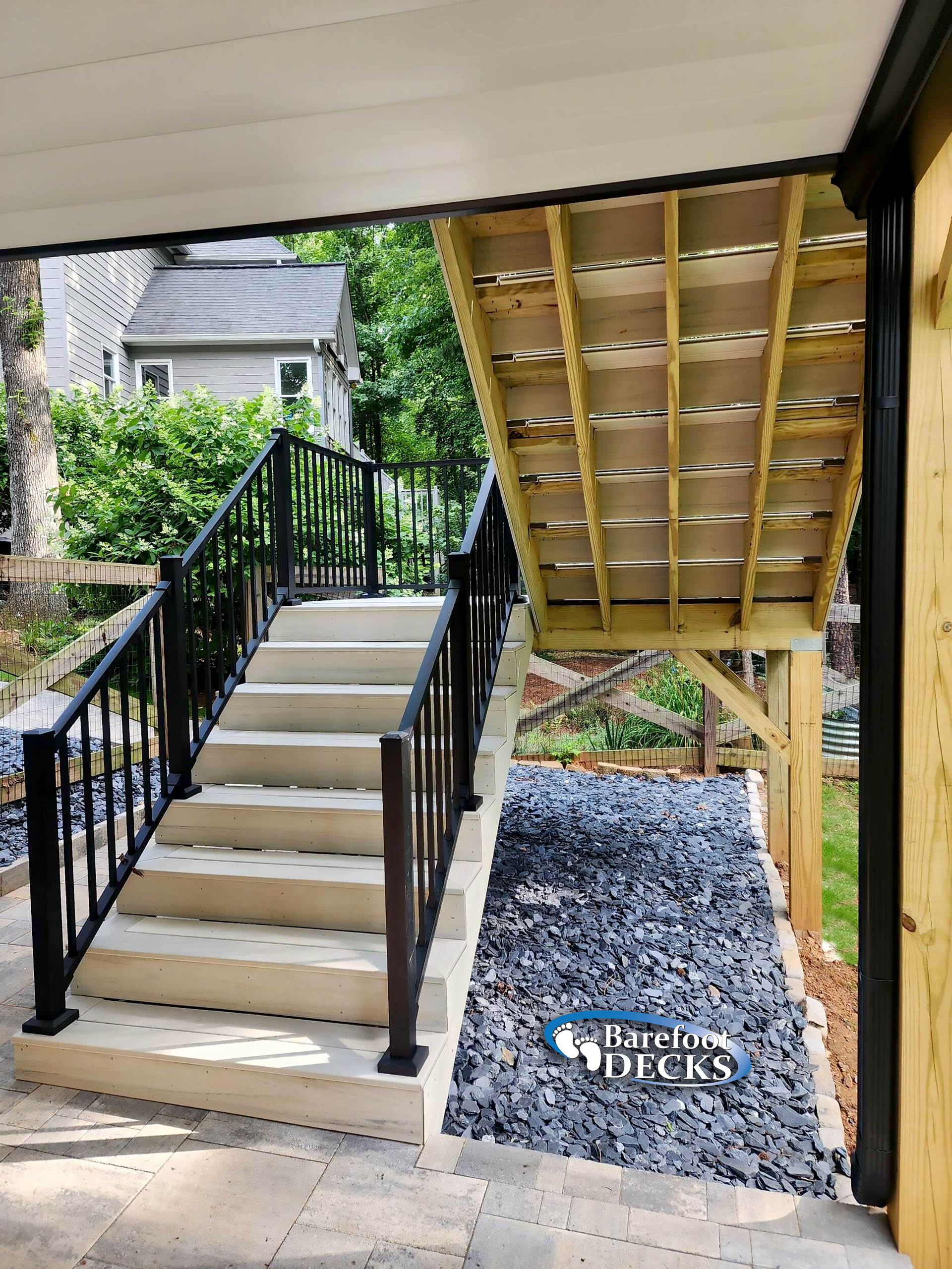 Stone steps with black railing leading up to a deck, beneath a deck with exposed wooden beams.