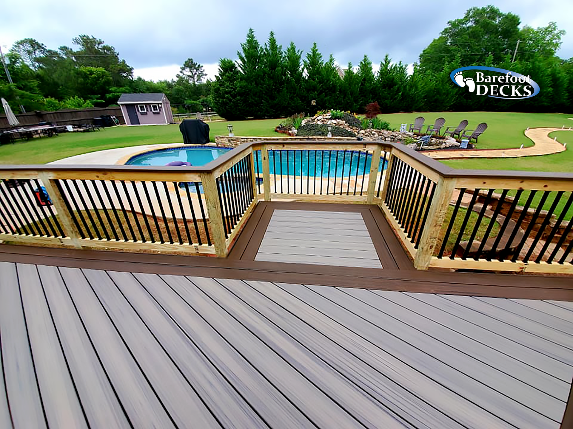 Composite deck with a pool view, bordered by railing. Grass yard, trees, and sky in background.