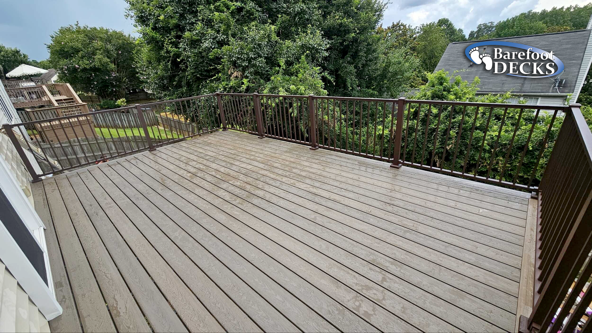 Wooden deck with brown railings, overlooking trees and a house.