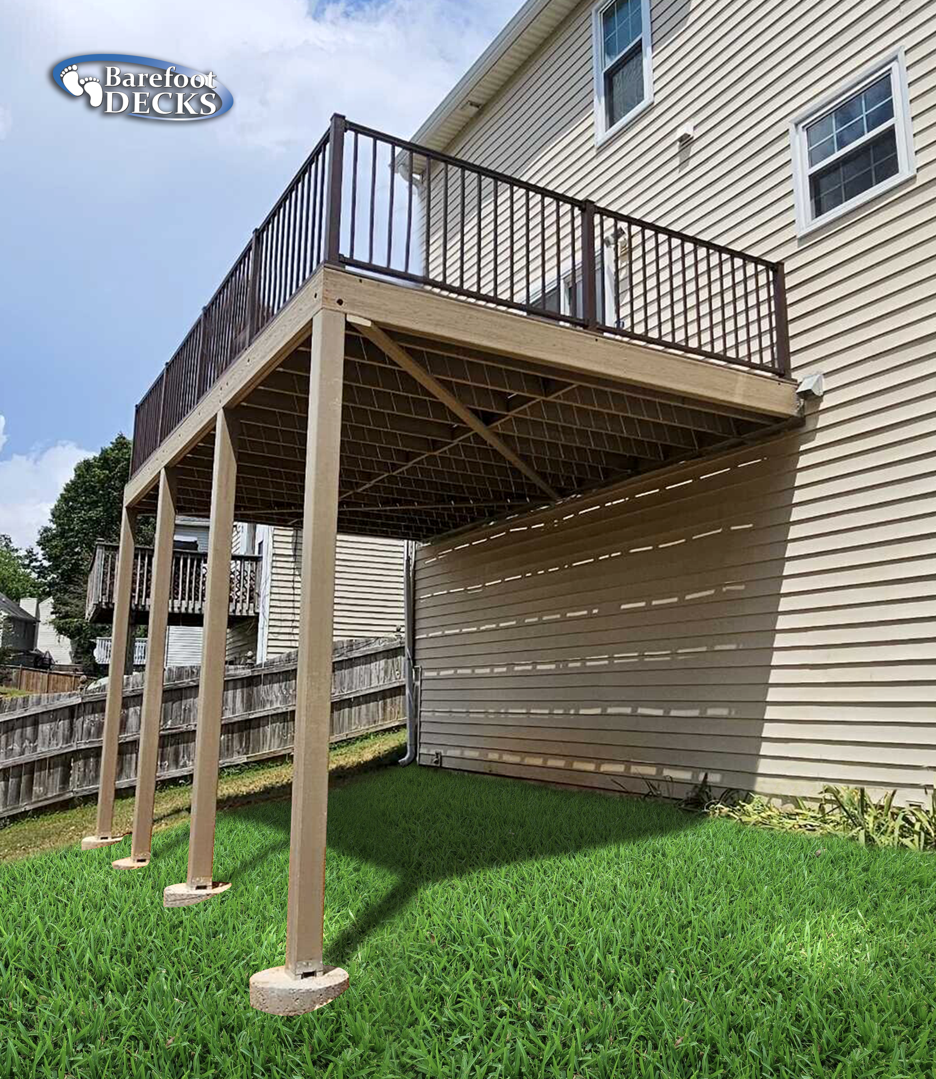 Elevated deck with brown railing and supports, over a grassy yard, attached to a light-colored house.