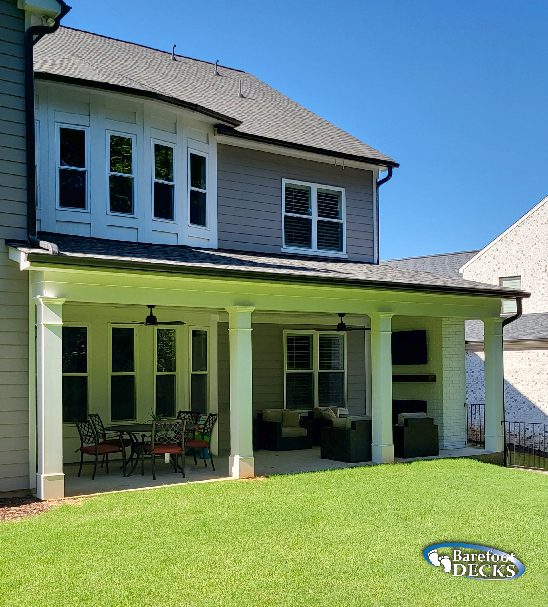 Backyard patio with columns, dining set, and lawn under a blue sky.