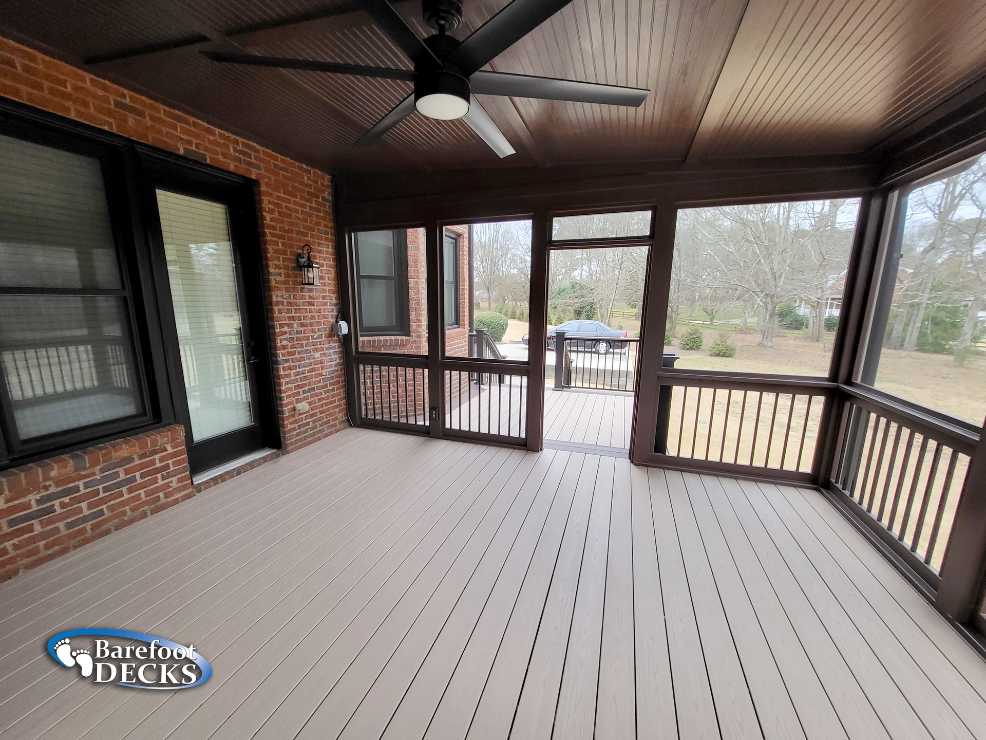 Screened porch with brown trim, beige floorboards, brick wall, and a ceiling fan.