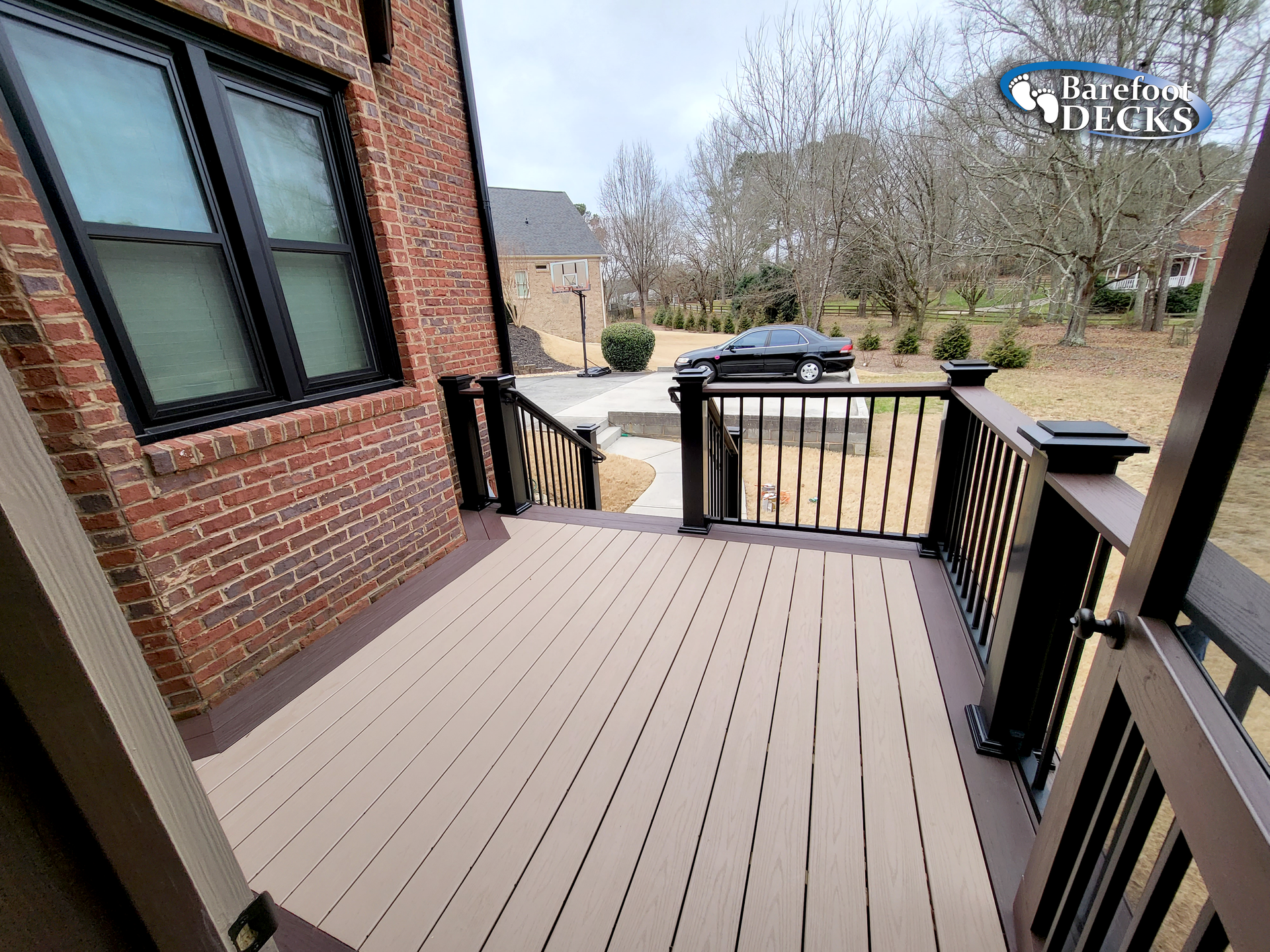 Composite deck with brown boards, dark railing, and brick house.