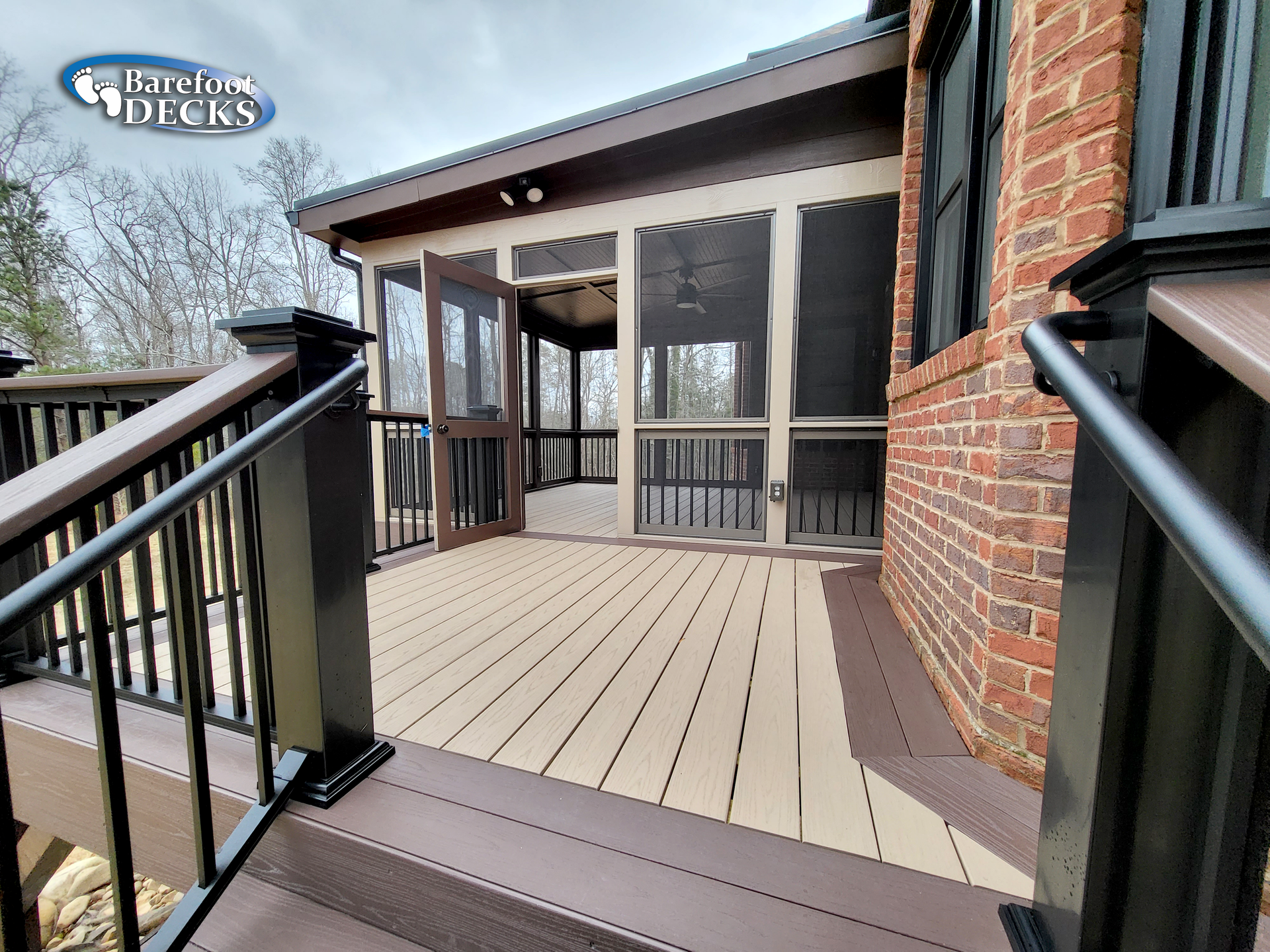 Composite deck with black railing and screened porch next to a brick house.