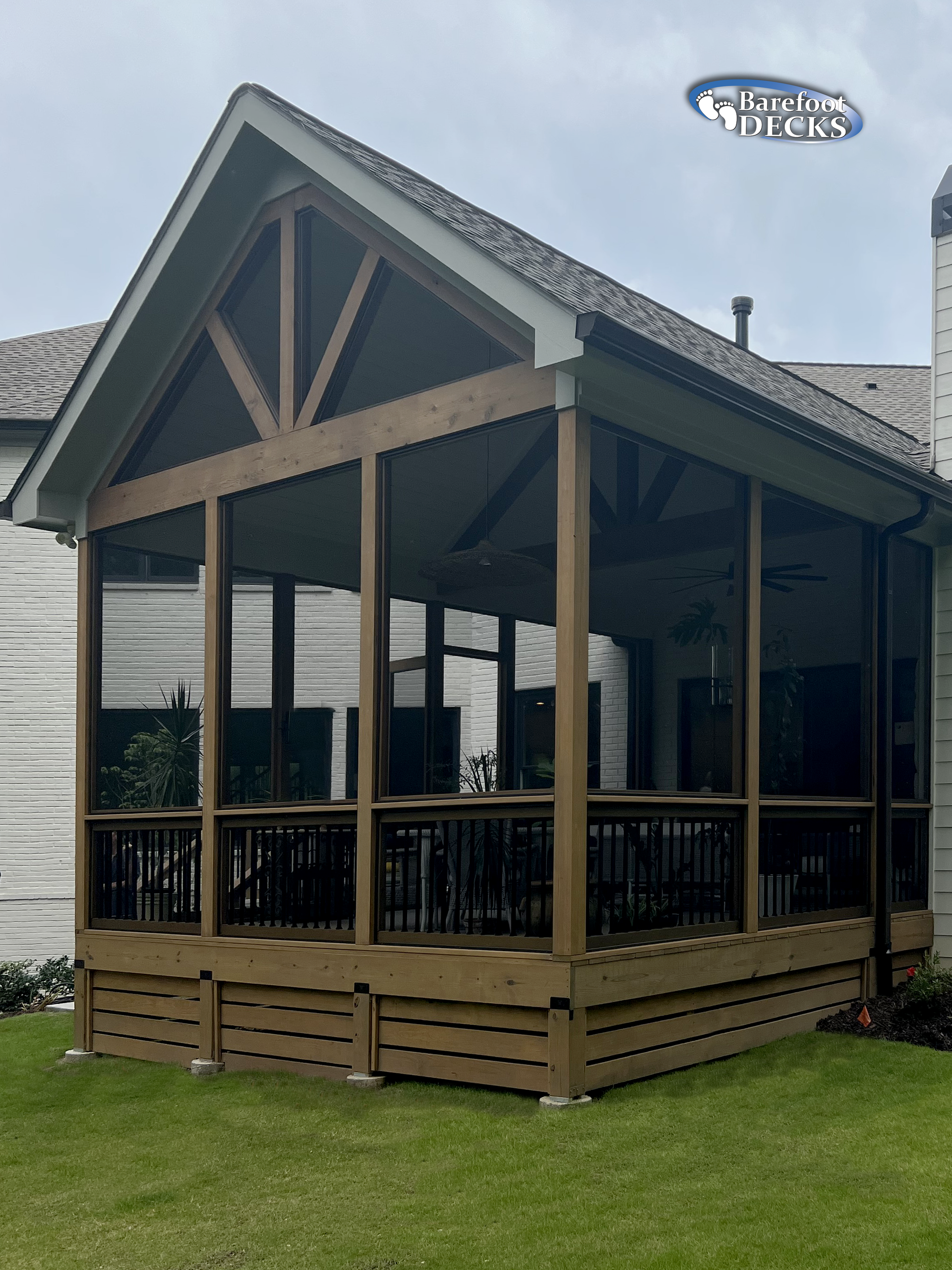 Screened-in porch addition with wood framing, dark screens, and a composite deck; attached to a house with a green lawn.