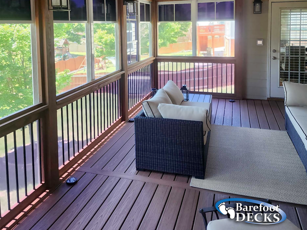 Covered porch with wicker sofa, striped rug, wood floor, and screened railings overlooking a yard