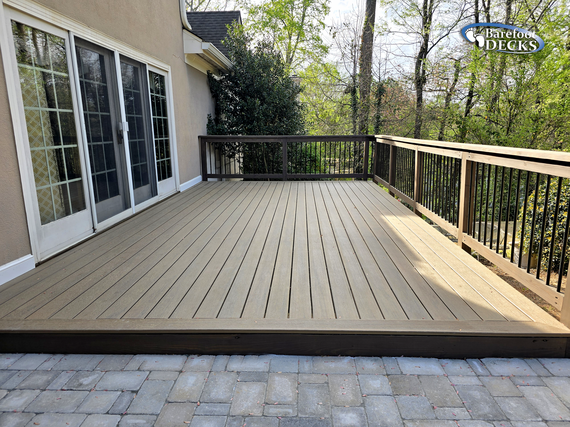 Spacious wooden deck with black railing beside a house, overlooking a wooded backyard.