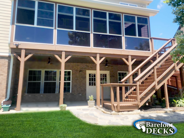 Two-story house with screened upper porch, stone lower level, and wooden exterior staircase in a sunny yard